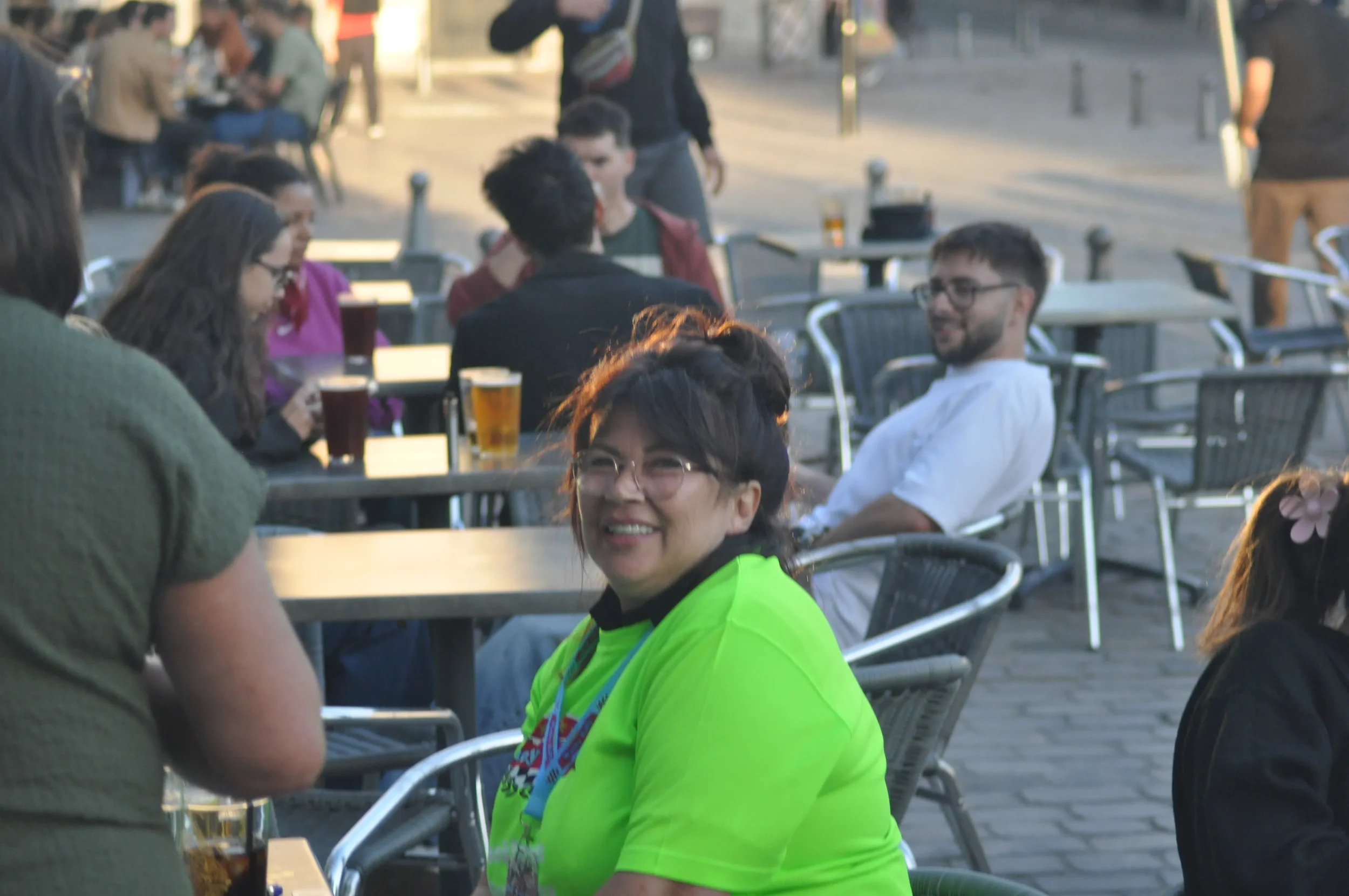 People sitting at an outdoor cafe, some drinking beer, enjoying a social gathering in the evening.