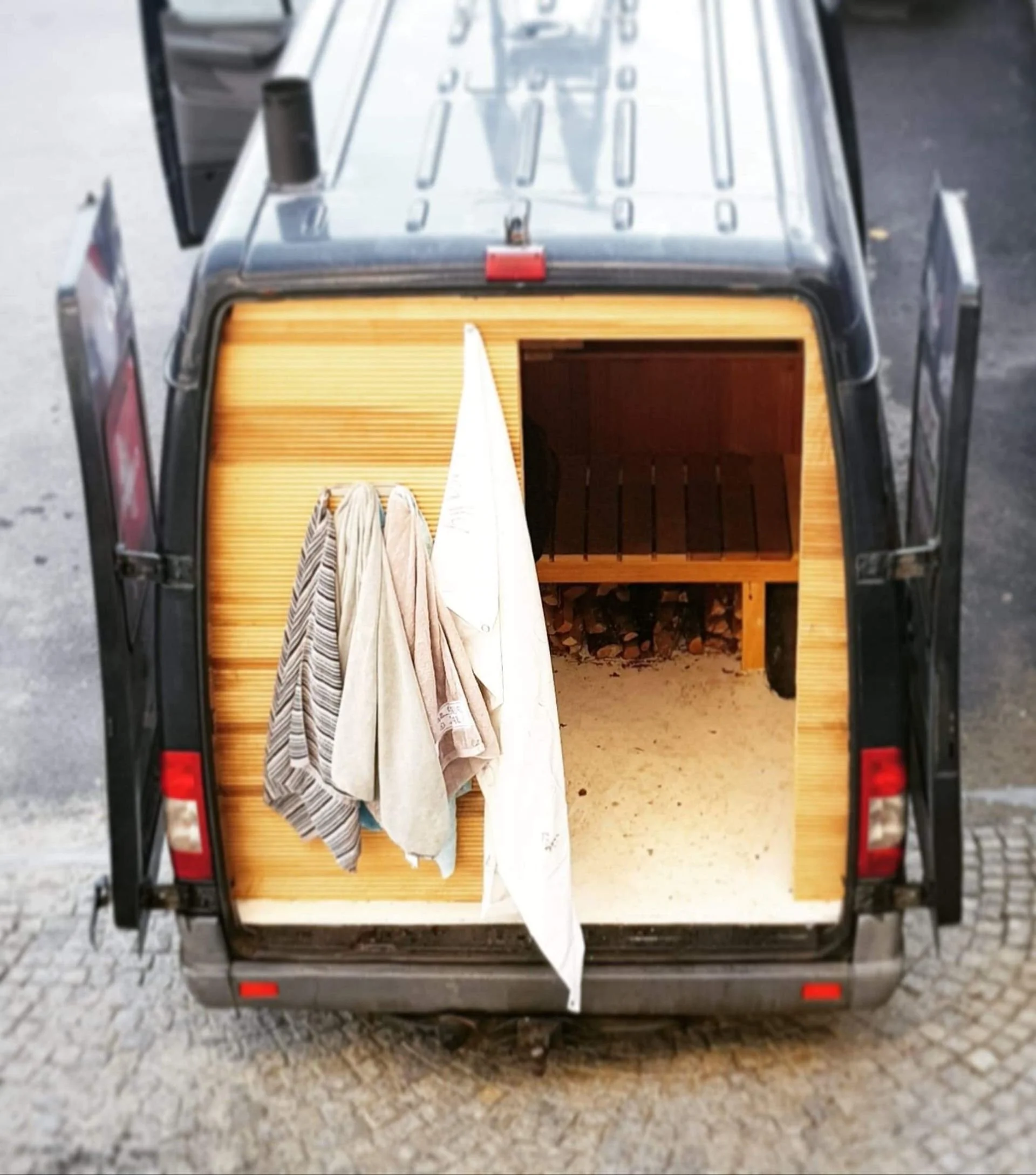 The back of a small mobile food or service cart with a wooden interior, hanging towels, and a small wooden bench or storage area.
