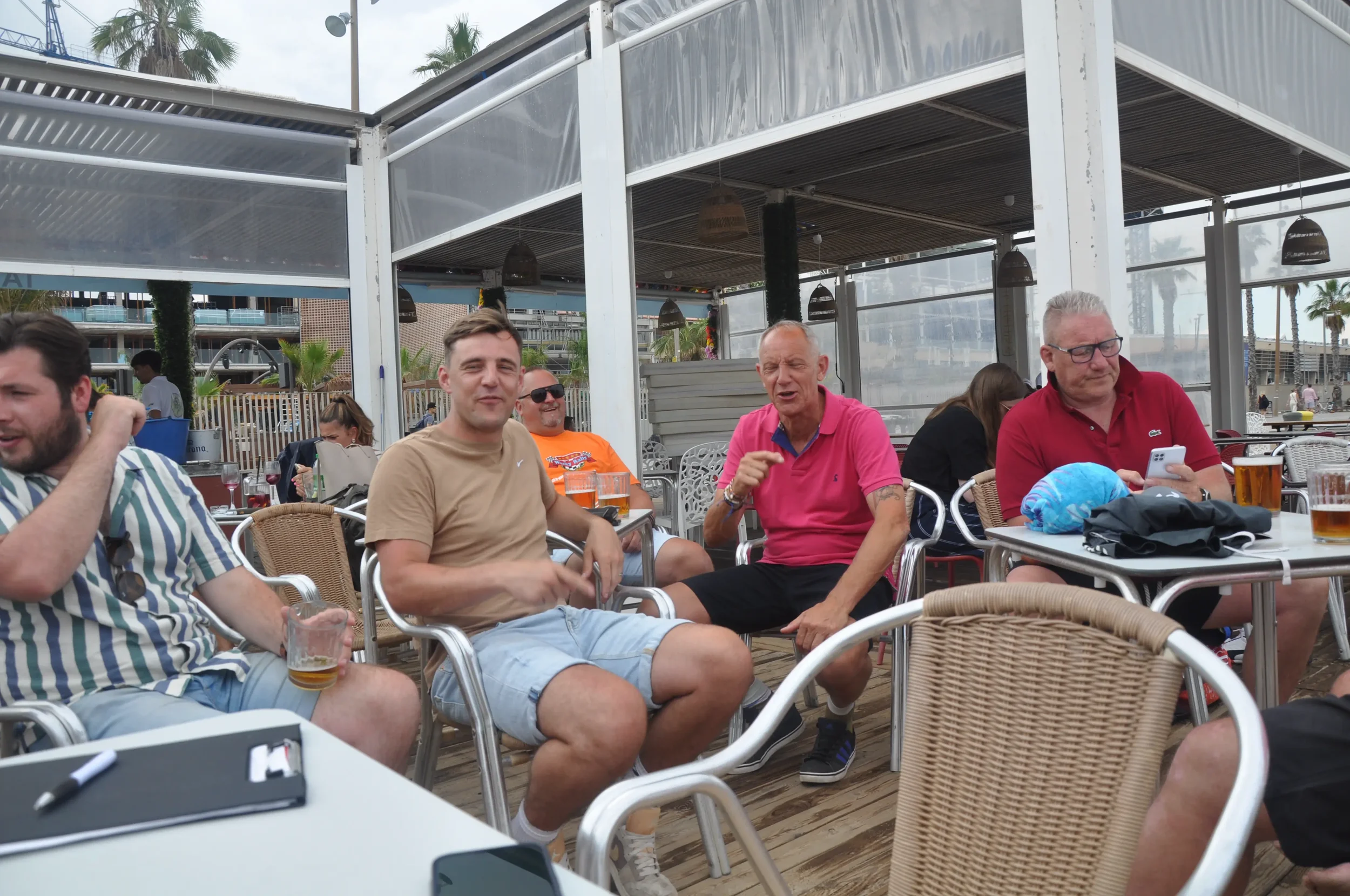 Group of men sitting at a table outside, enjoying drinks and conversation.
