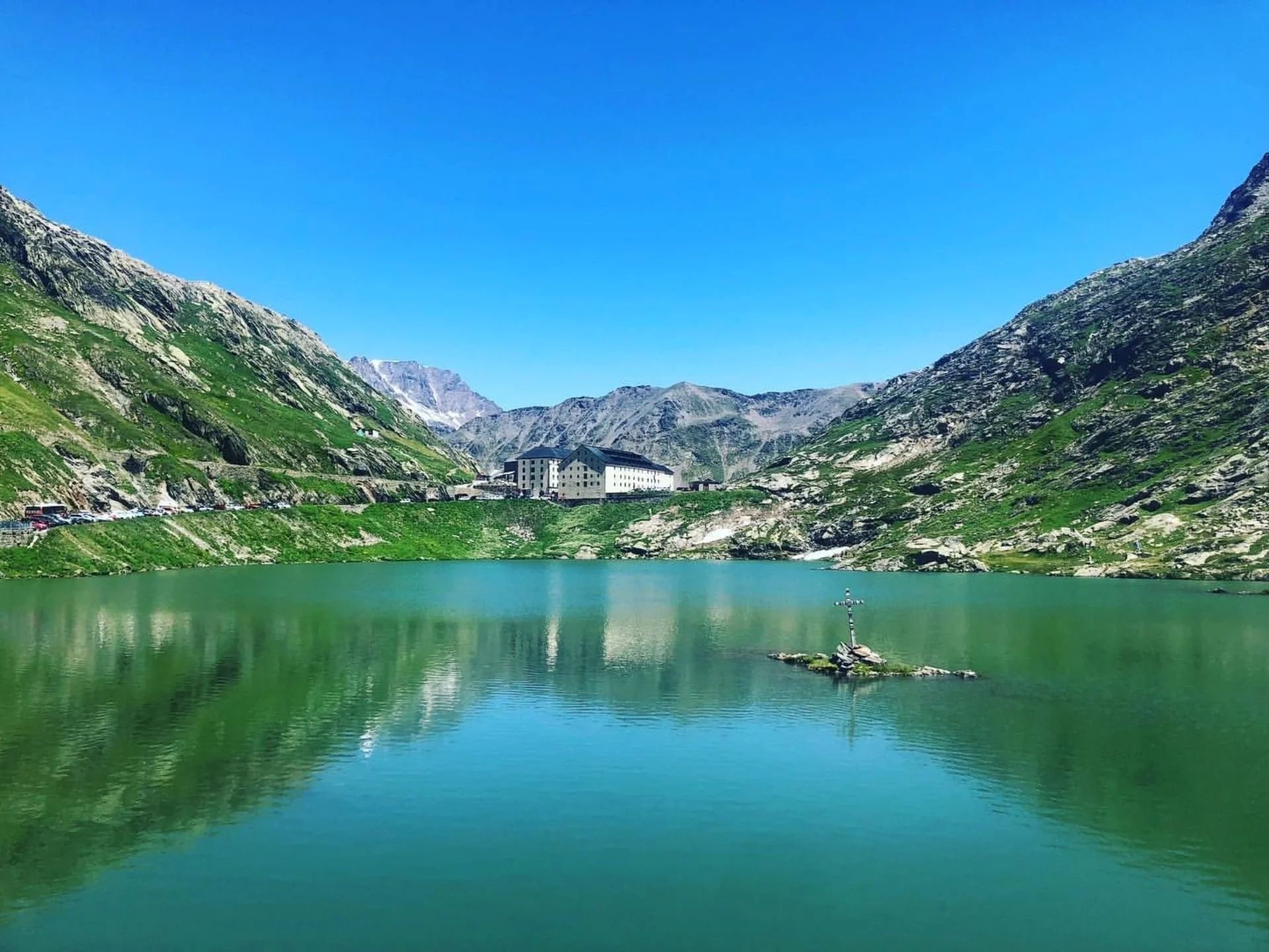 A mountain lake with green waters surrounded by green and rocky mountain slopes under a clear blue sky.