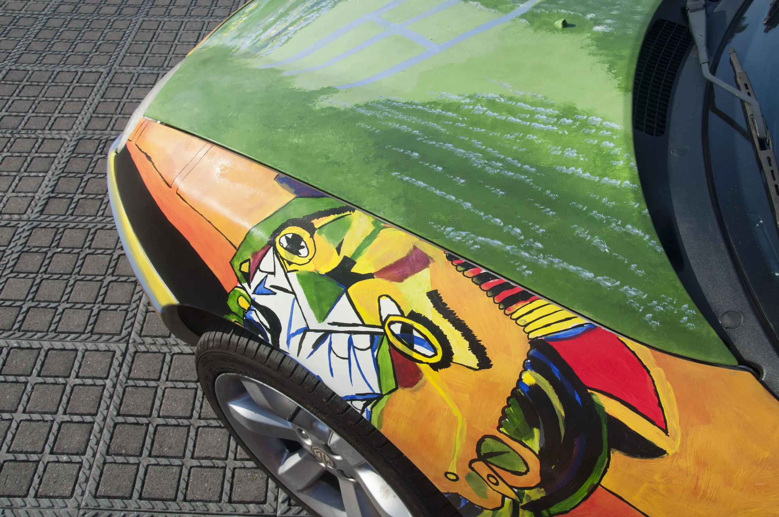 Car with colorful, abstract artwork on the hood, featuring a cartoonish character with large eyes and exaggerated features, set against a vibrant, multi-colored background.