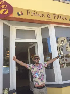 Person standing in front of a French fry and pastry shop with arms outstretched