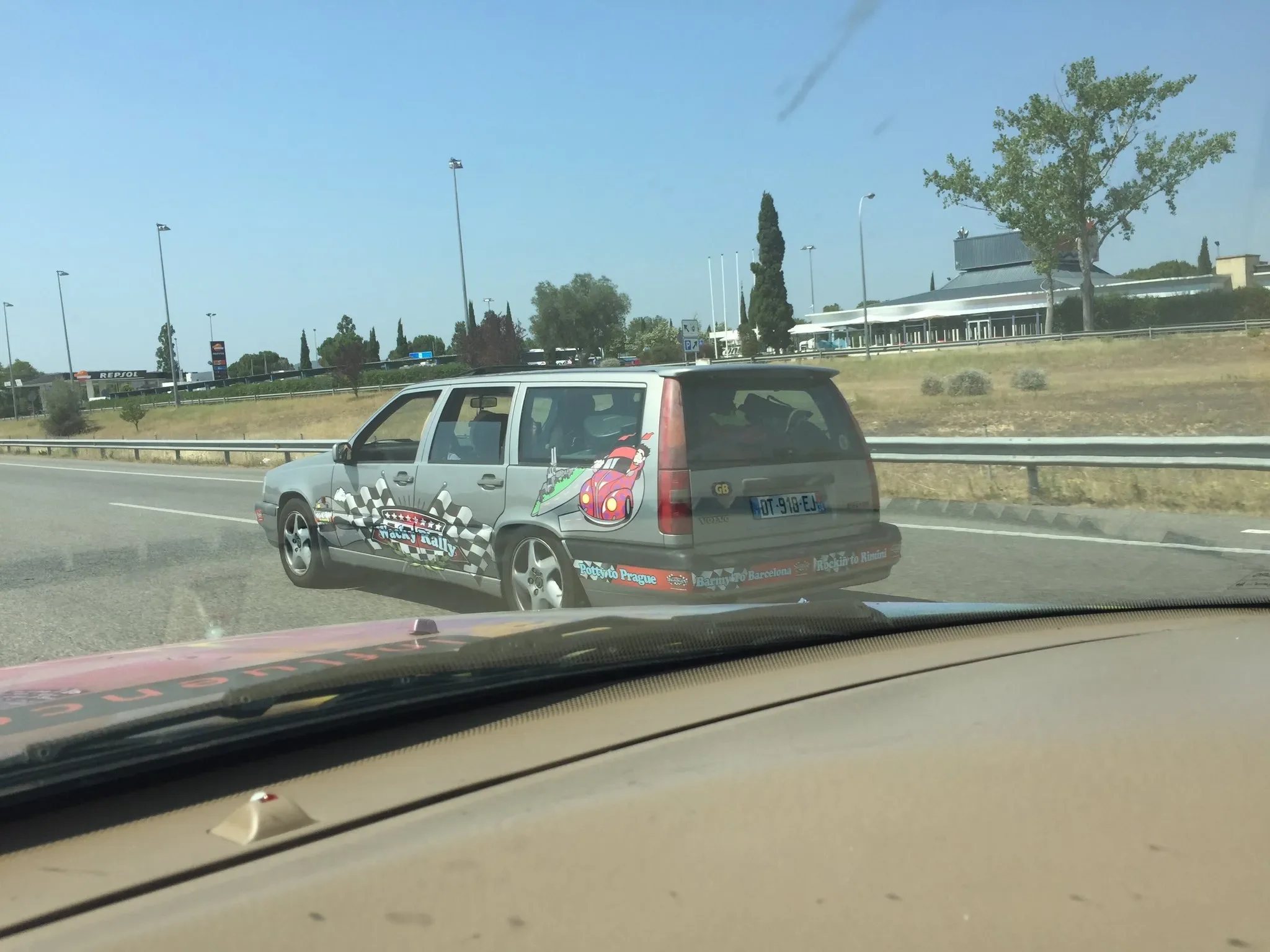 A station wagon decorated with racing-themed graphics driving on a highway. The car features cartoon characters and checkered flag patterns.