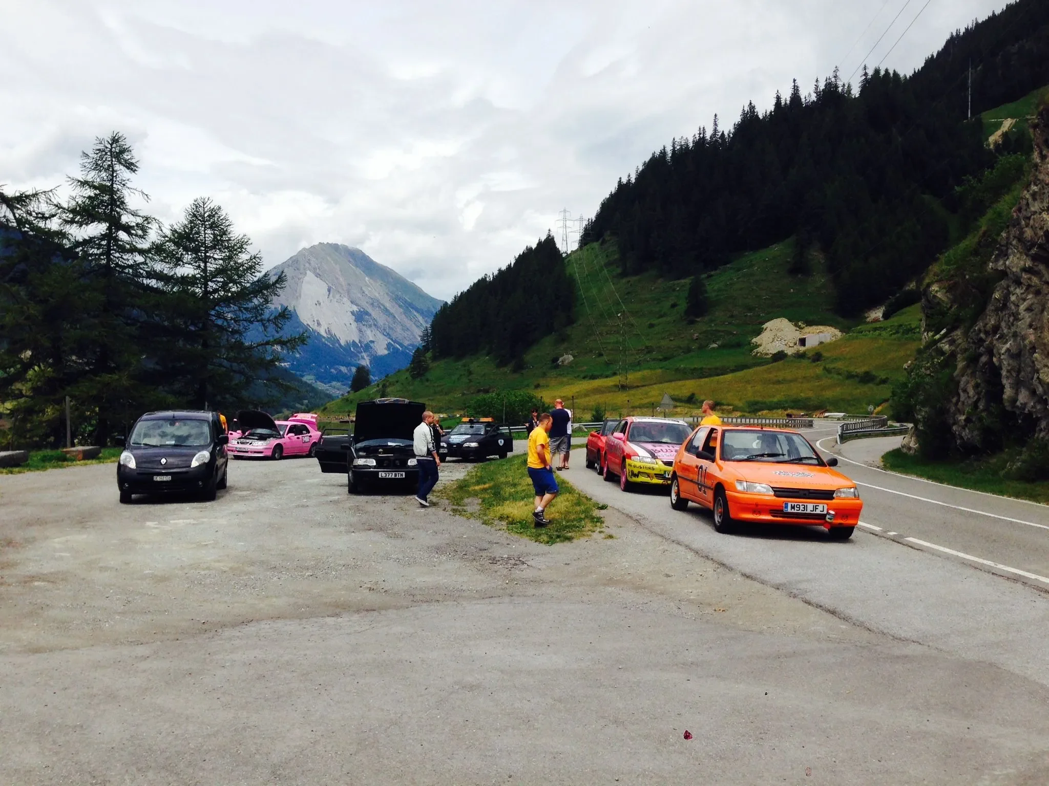 Mountain scenery with parked cars and a few people in a roadside rest area.