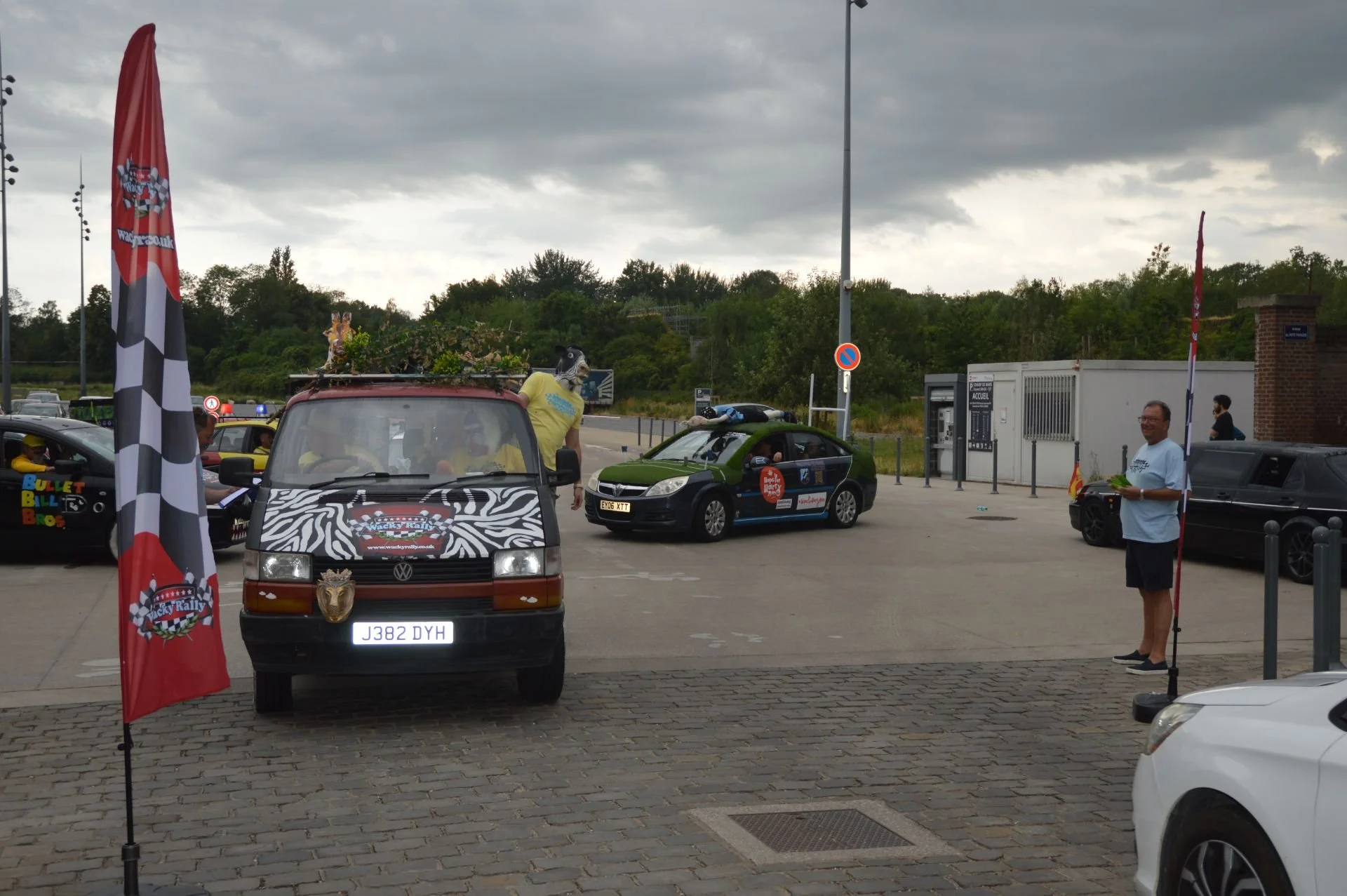A parking lot during the day with decorated cars and flags for a rally event, with a cloudy sky overhead.