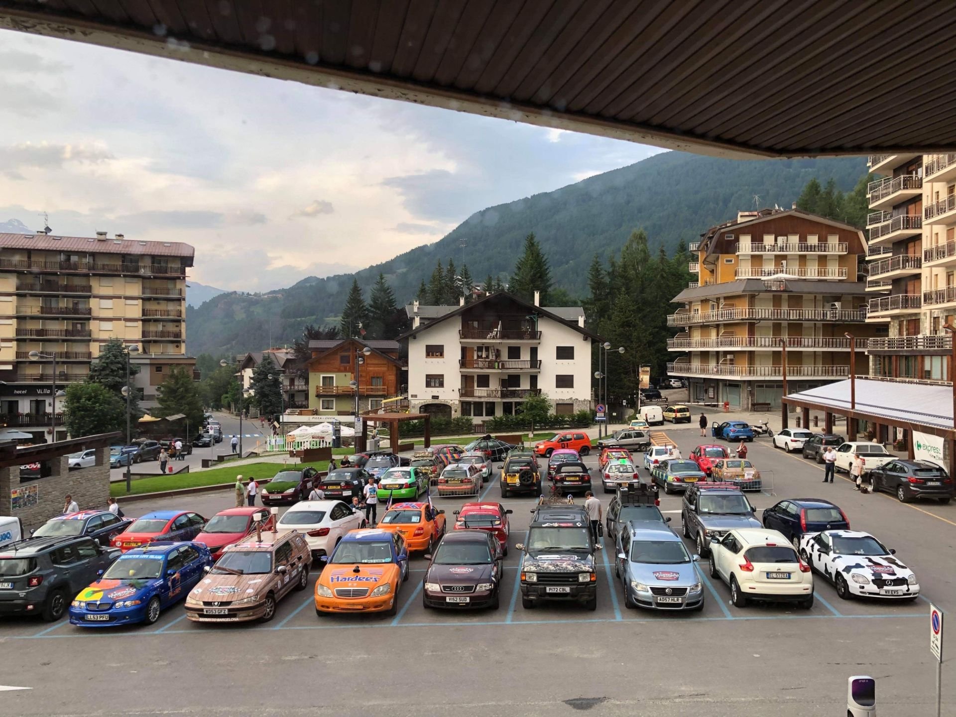 A parking lot filled with cars in front of buildings and mountains in the background.