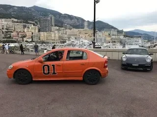 Orange toy car with the number 01 on its side, parked in front of a cityscape with mountains in the background.