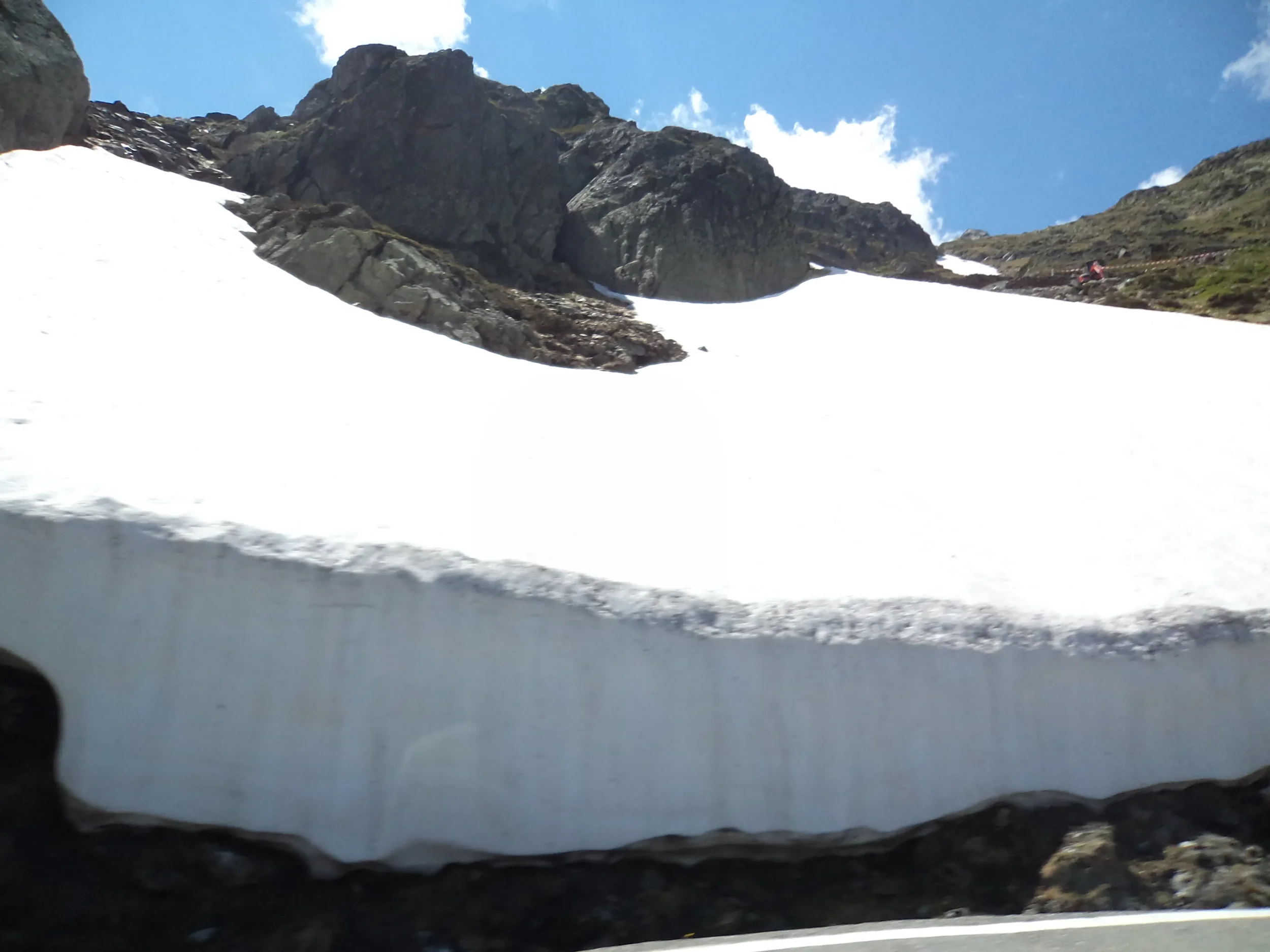 Snow-covered mountain slope with rocky peaks and a blue sky with a few clouds.