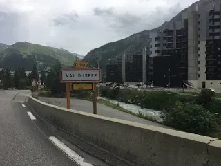 Road sign indicating the town of Val di Isere with mountains and buildings in the background.