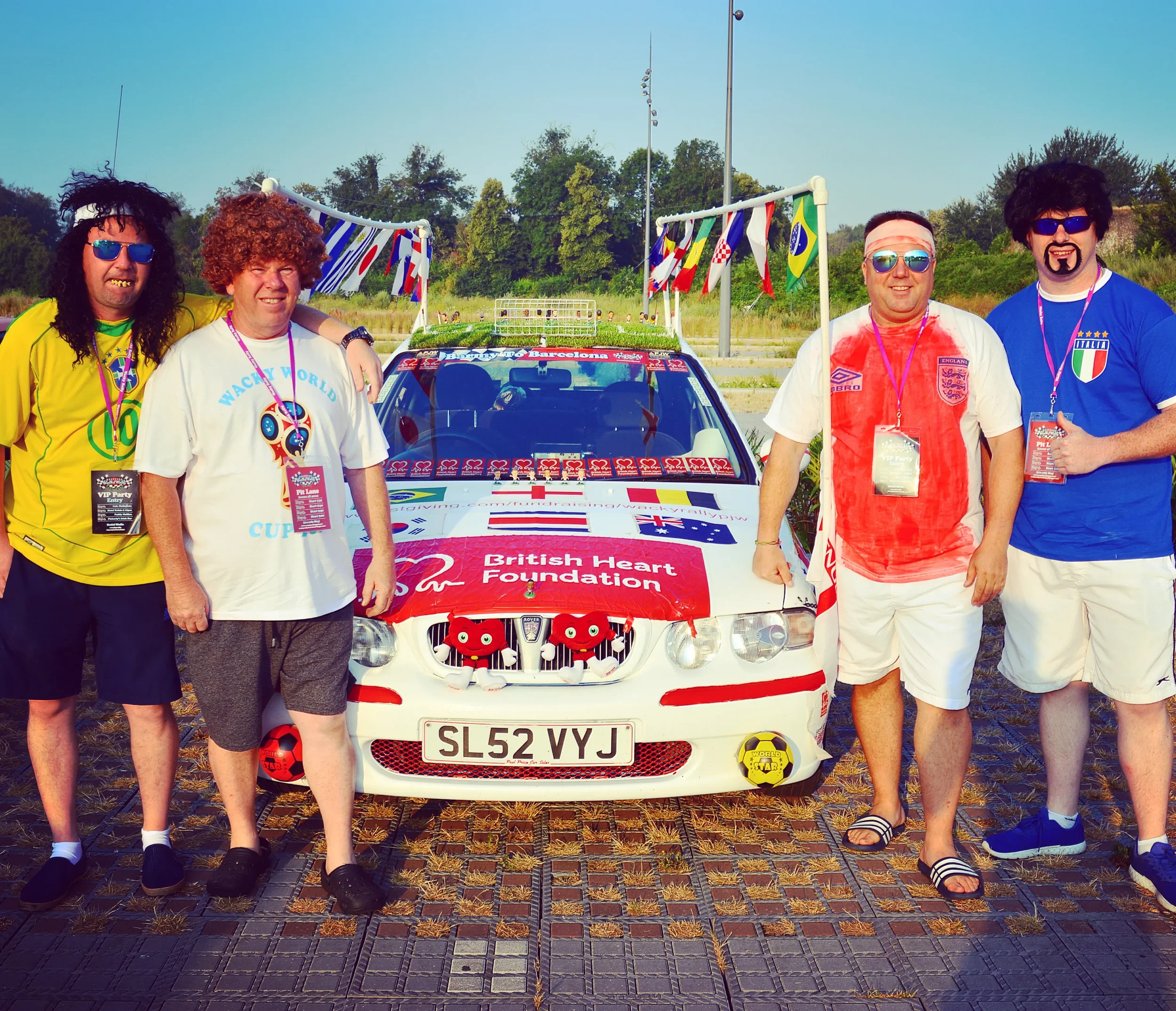 Group of five men dressed in soccer fan attire posing next to a decorated rally car with flags and sponsorship stickers at an outdoor event.