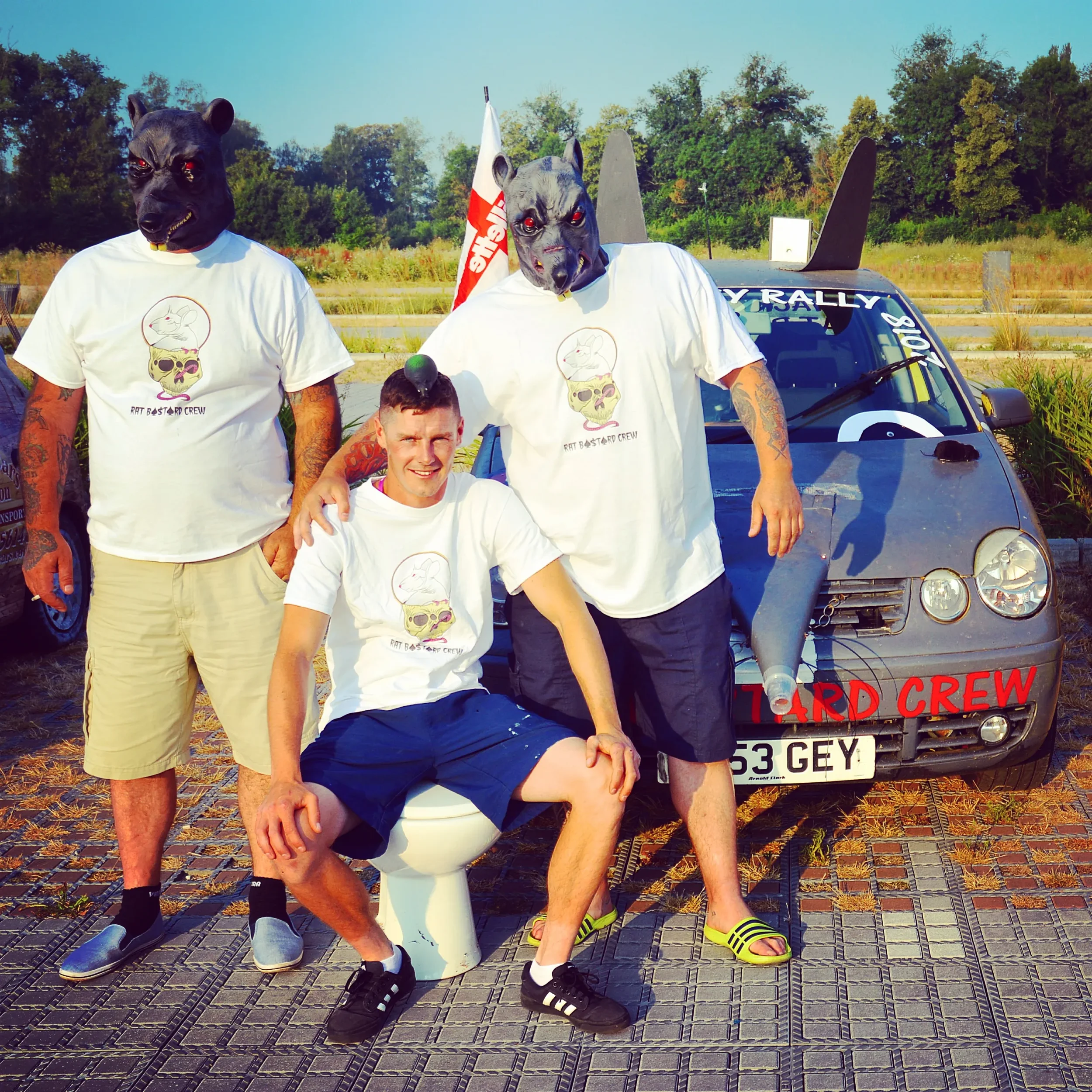 Four men, some wearing dog masks and matching t-shirts, pose in front of a car with a 'Hard Crew' sign. One man is sitting on a toilet seat, and a flag is visible in the background.