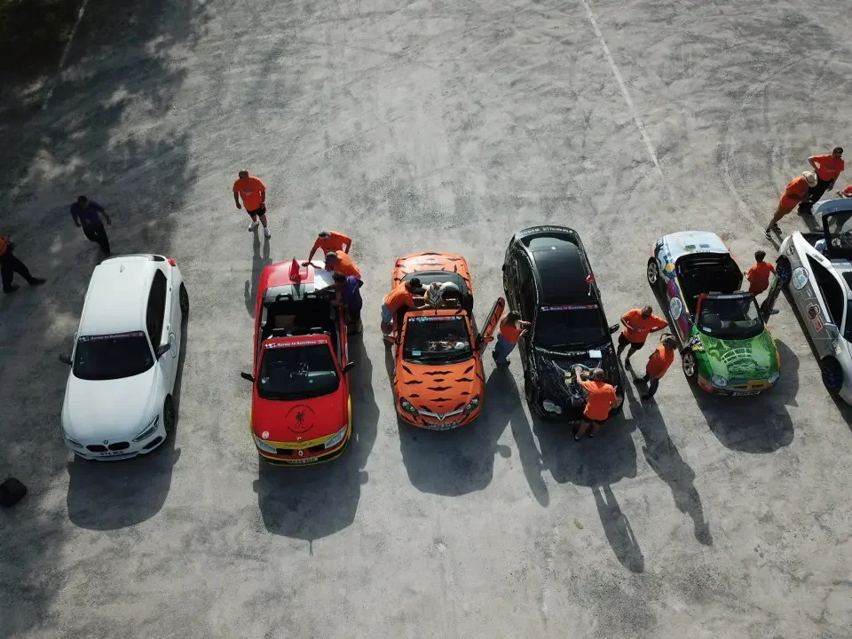 Group of race car drivers and crew preparing their cars in a pit area.