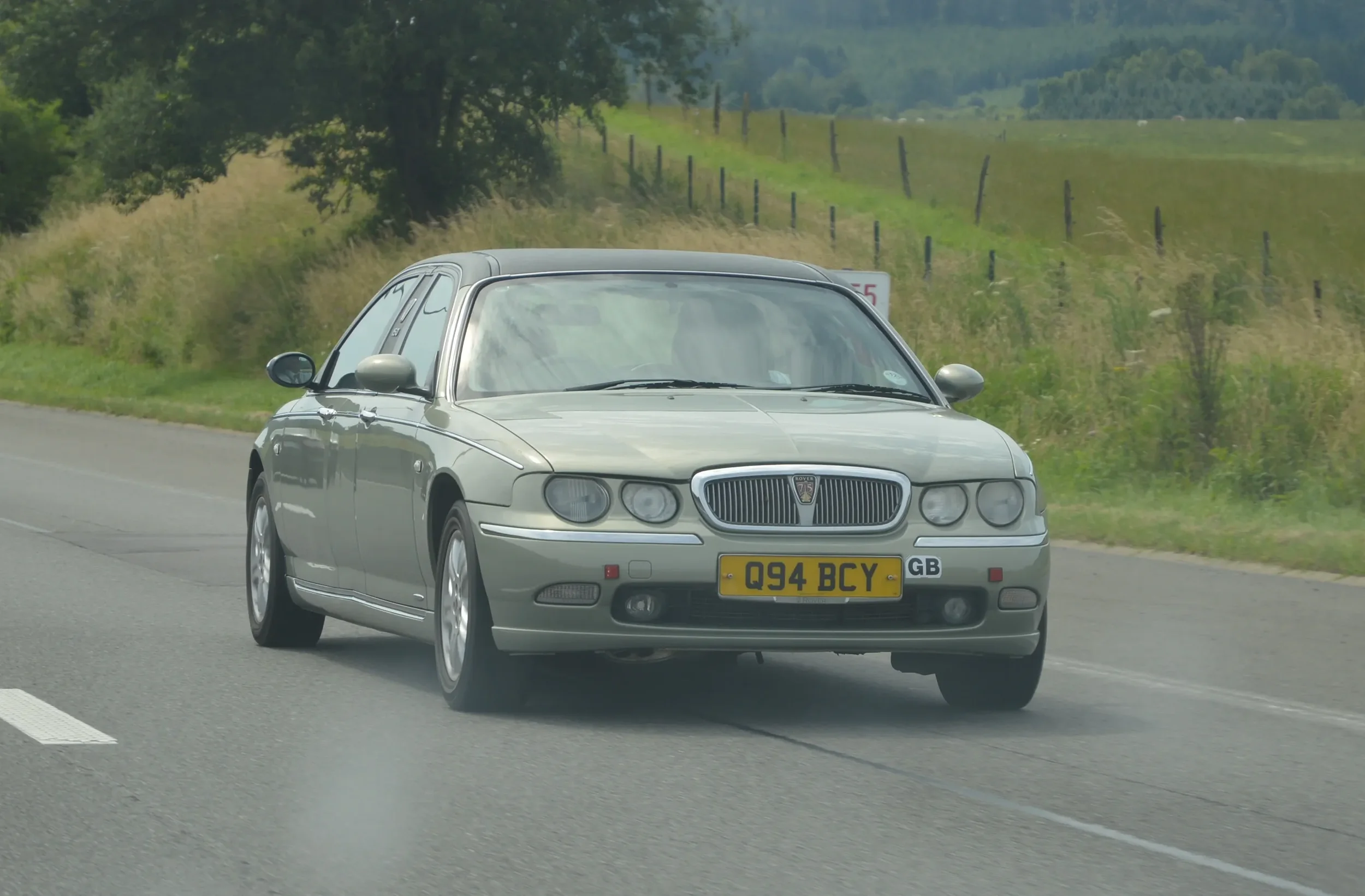 Silver Rover 75 sedan driving on a highway with grassy fields and trees in the background.