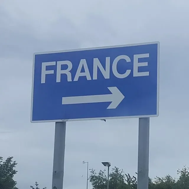 Blue road sign with white text that says "FRANCE" and a right-pointing arrow, indicating the direction to France.