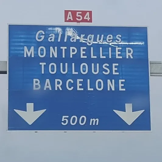 A French highway road sign listing cities Gallargues, Montpellier, Toulouse, and Barcelone, with directions indicating 500 meters ahead.