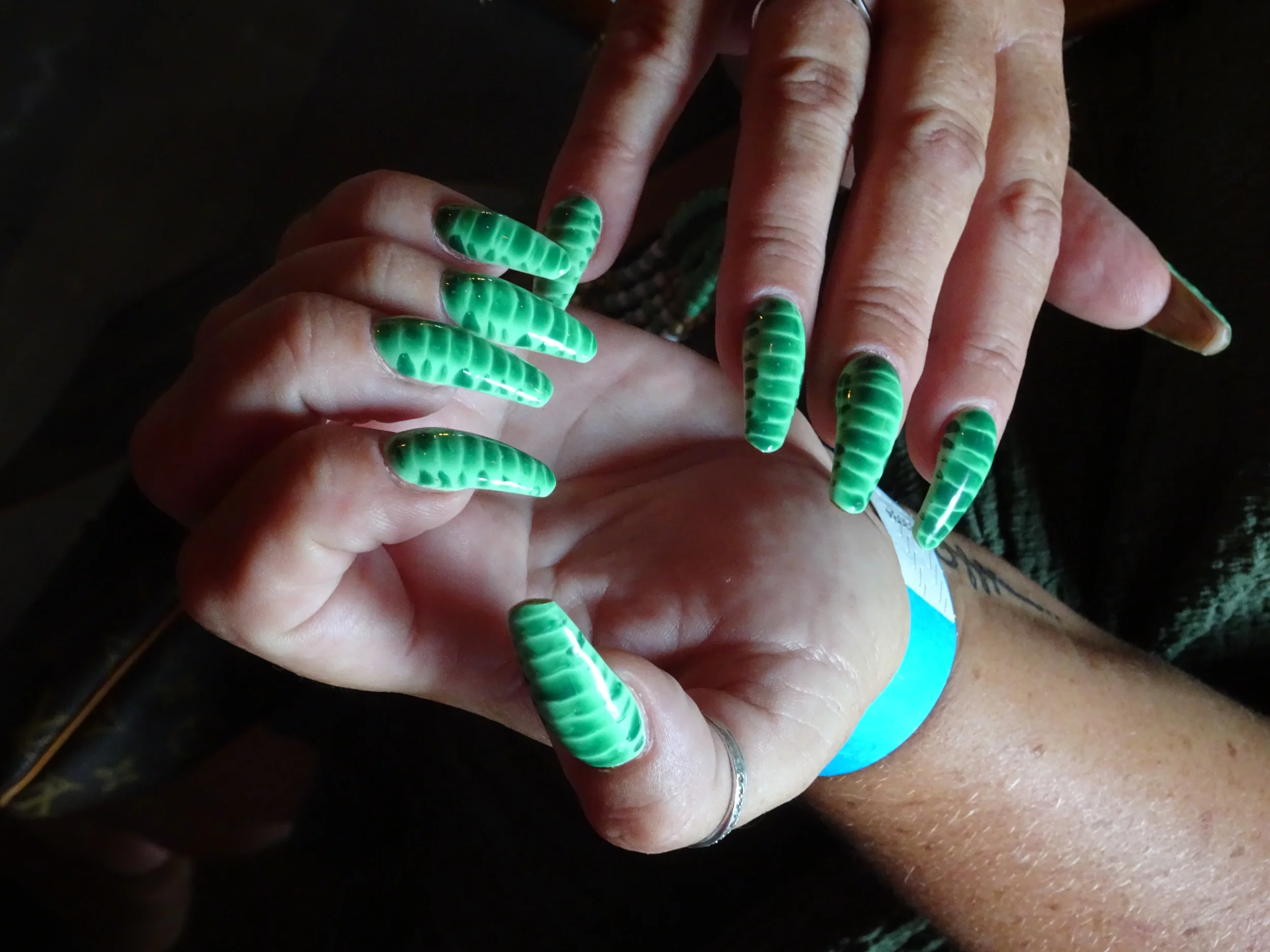 Close-up of a person's hands with long, green, manicured nails featuring a dark green stripe pattern.