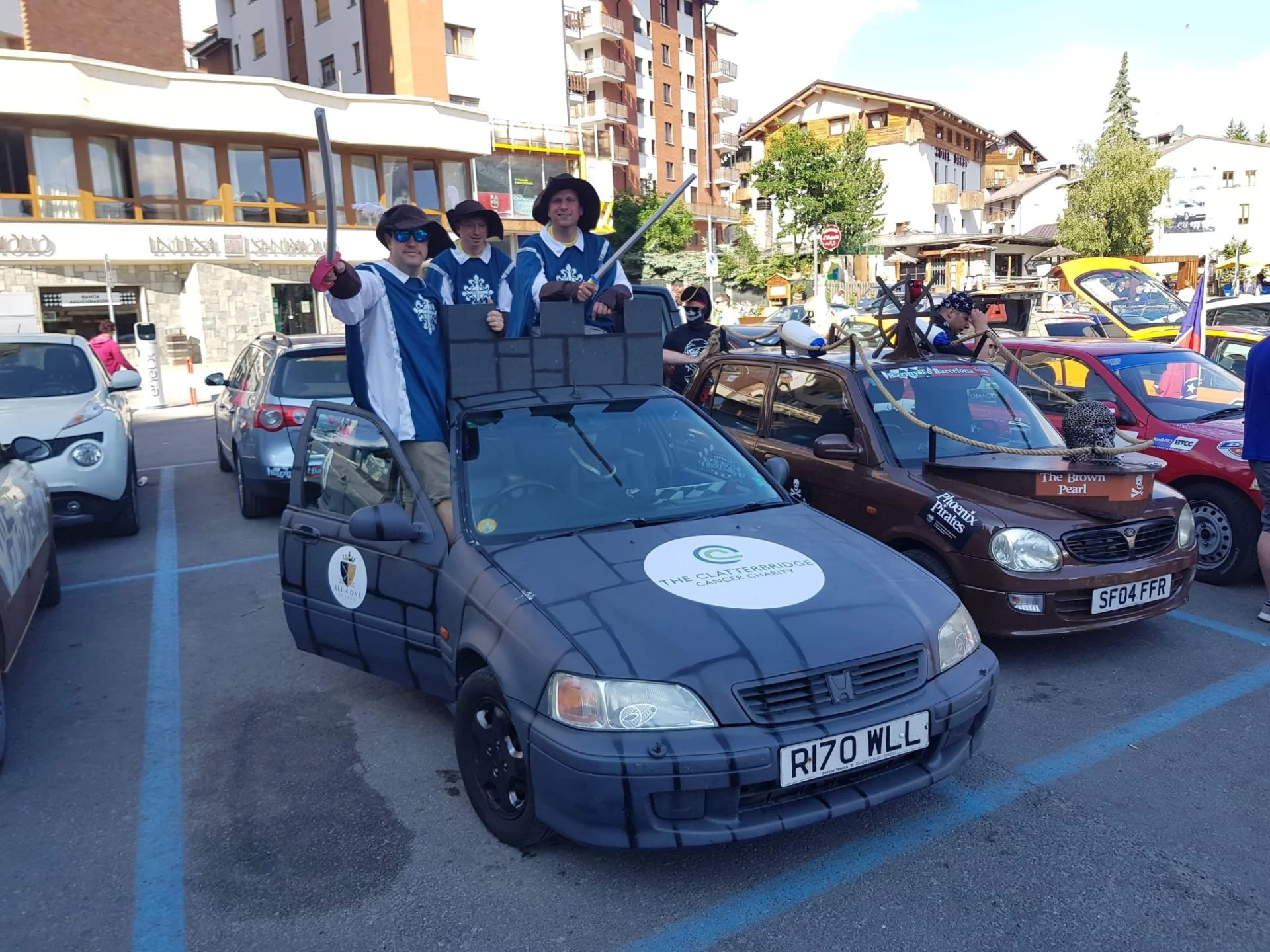 A group of people dressed as pirates standing on a car in a parking lot, with colorful buildings and cars in the background.