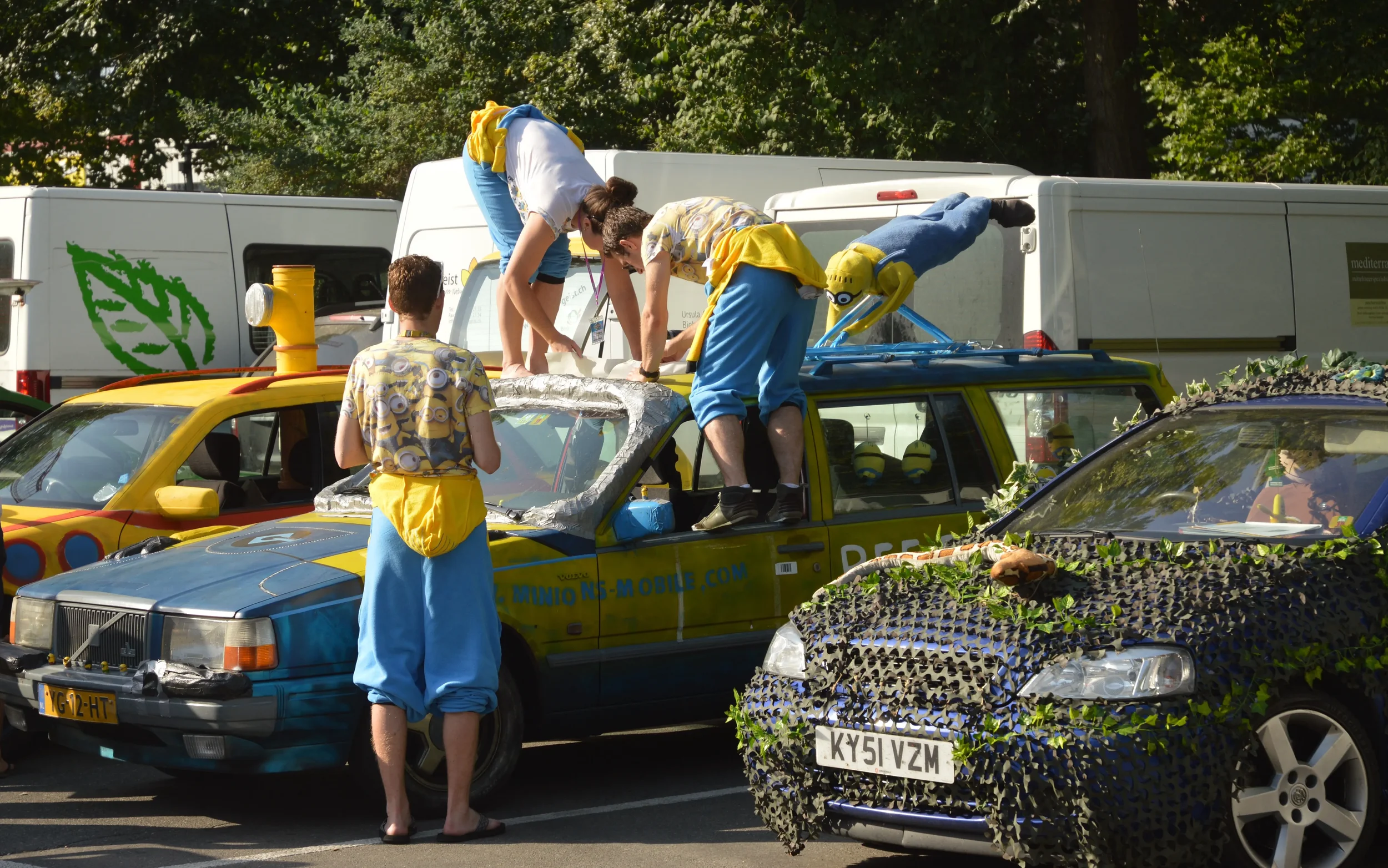 People dressed as Minions working on decorated cars in a parking lot.