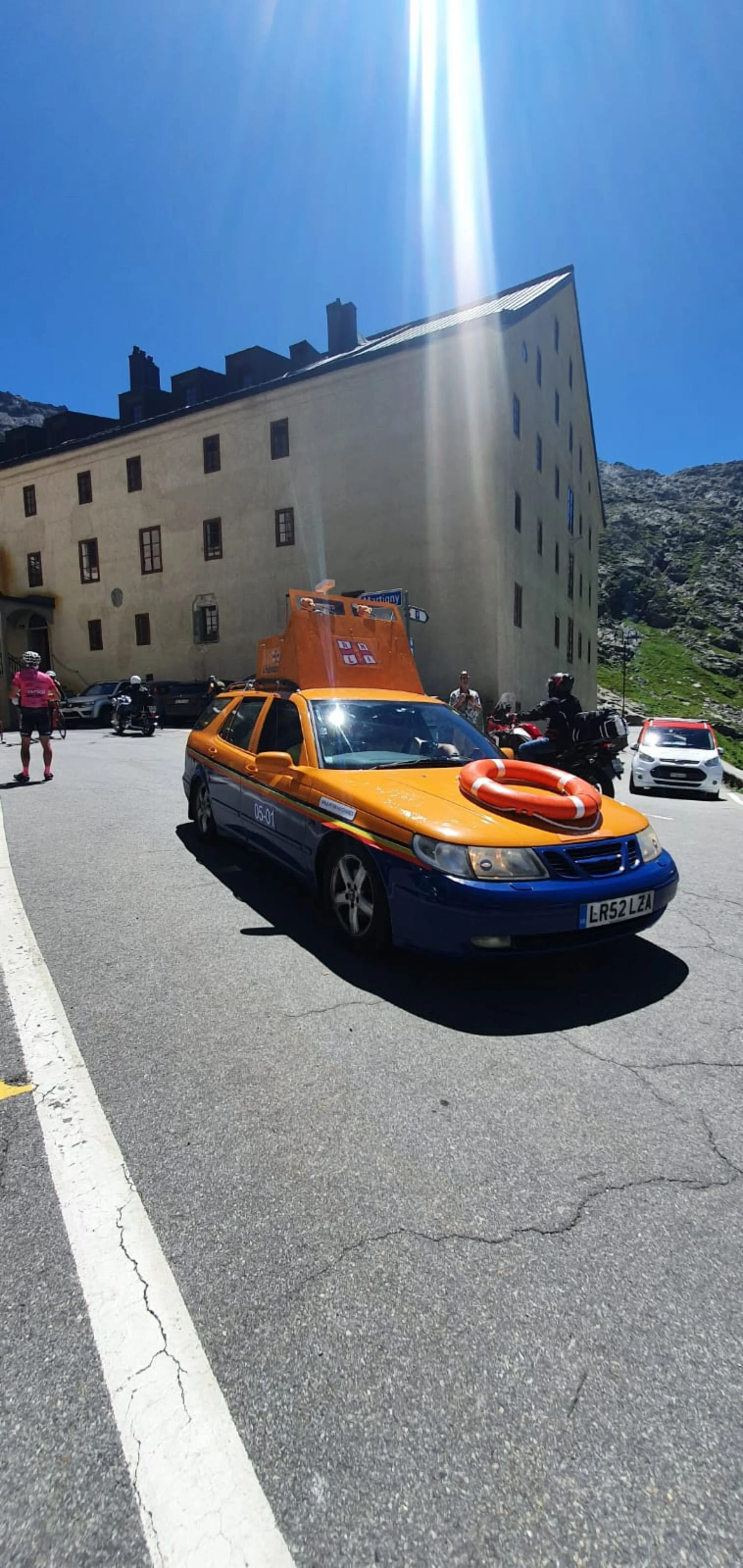 A yellow and blue emergency response vehicle with a life preserver on its hood, parked on a street in a mountainous area under a clear blue sky.