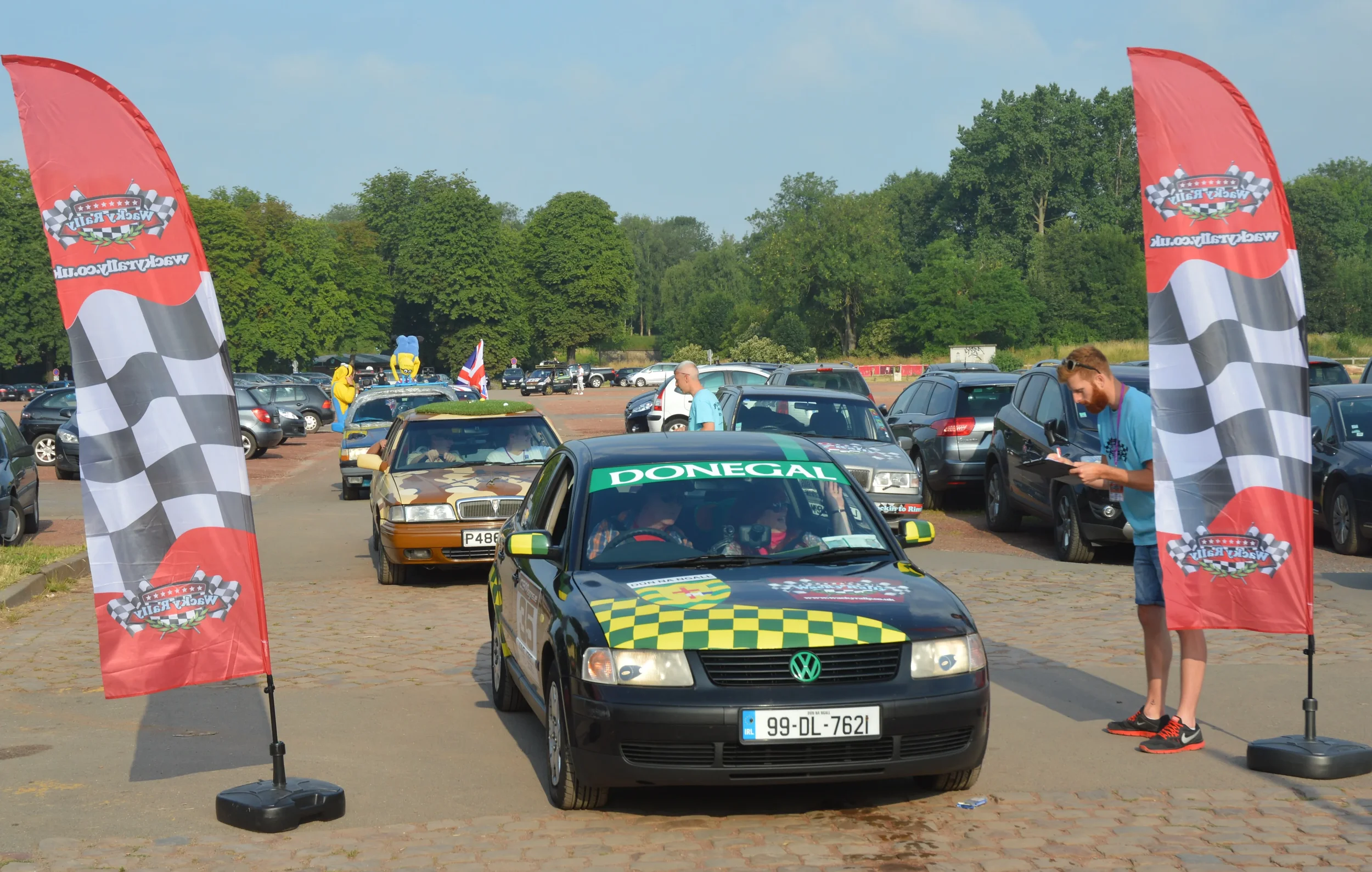 A racing event at a parking lot with checkered flags on poles, a Volkswagen car with Donegal signage, and people taking notes.