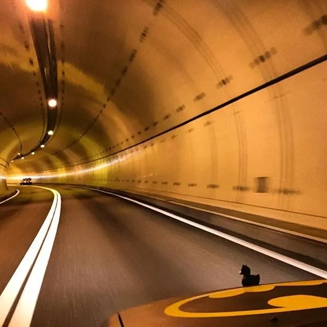 View of a tunnel from a moving vehicle, with the road curving to the right and vehicle headlights illuminating the tunnel walls.