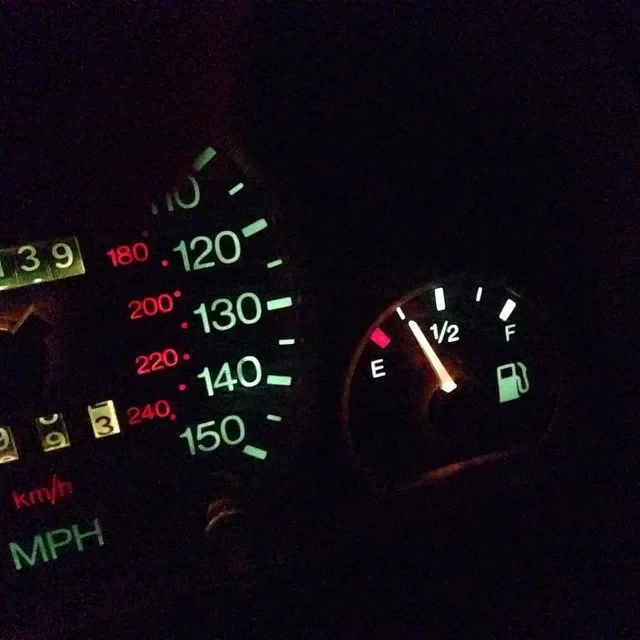 The image shows a car dashboard with the speedometer and fuel gauge. The speedometer needle points to approximately 20 MPH. The fuel gauge indicates the fuel level is just above empty, close to E.