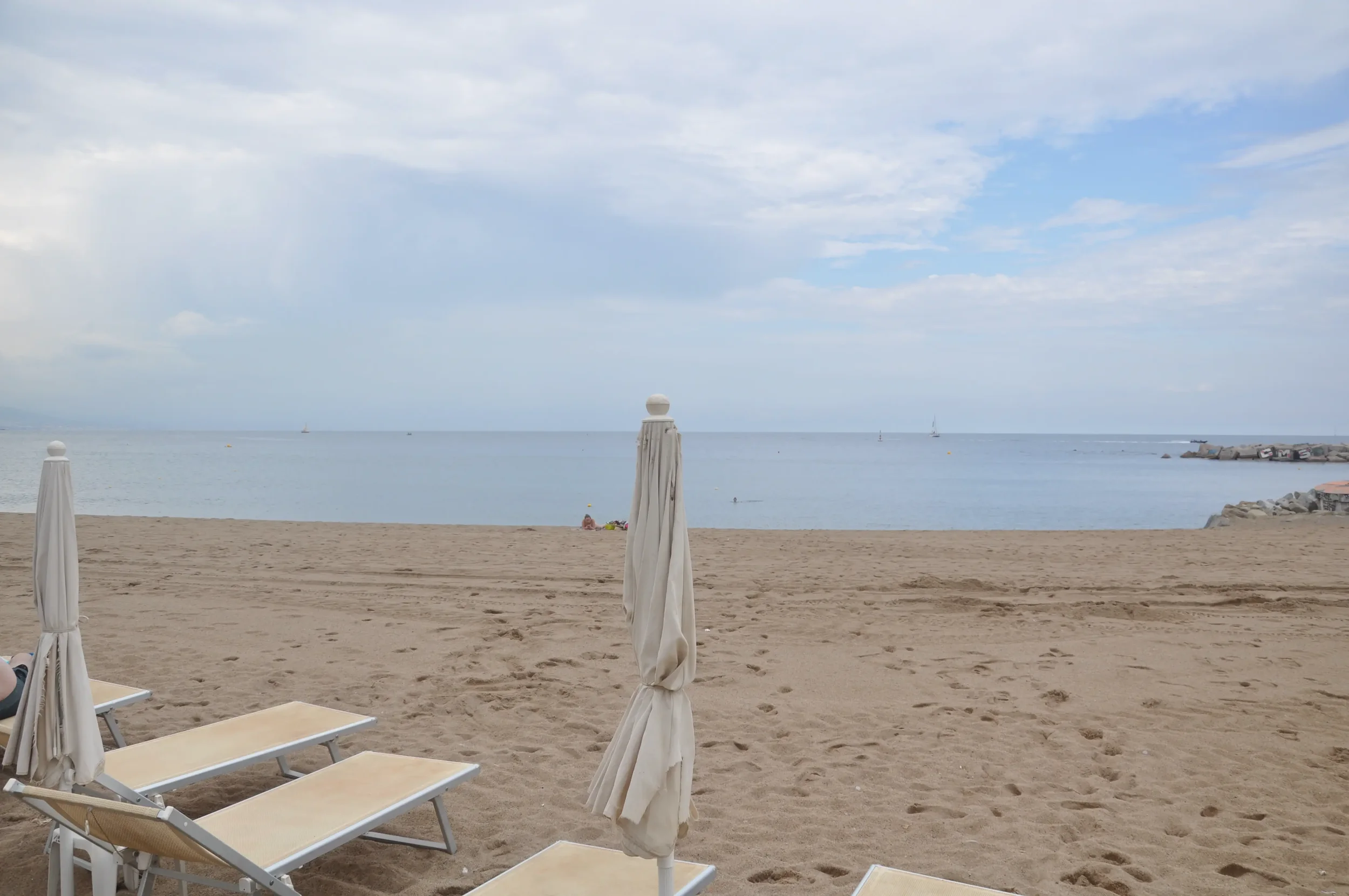 Empty beach chairs and umbrellas facing the ocean with a cloudy sky.