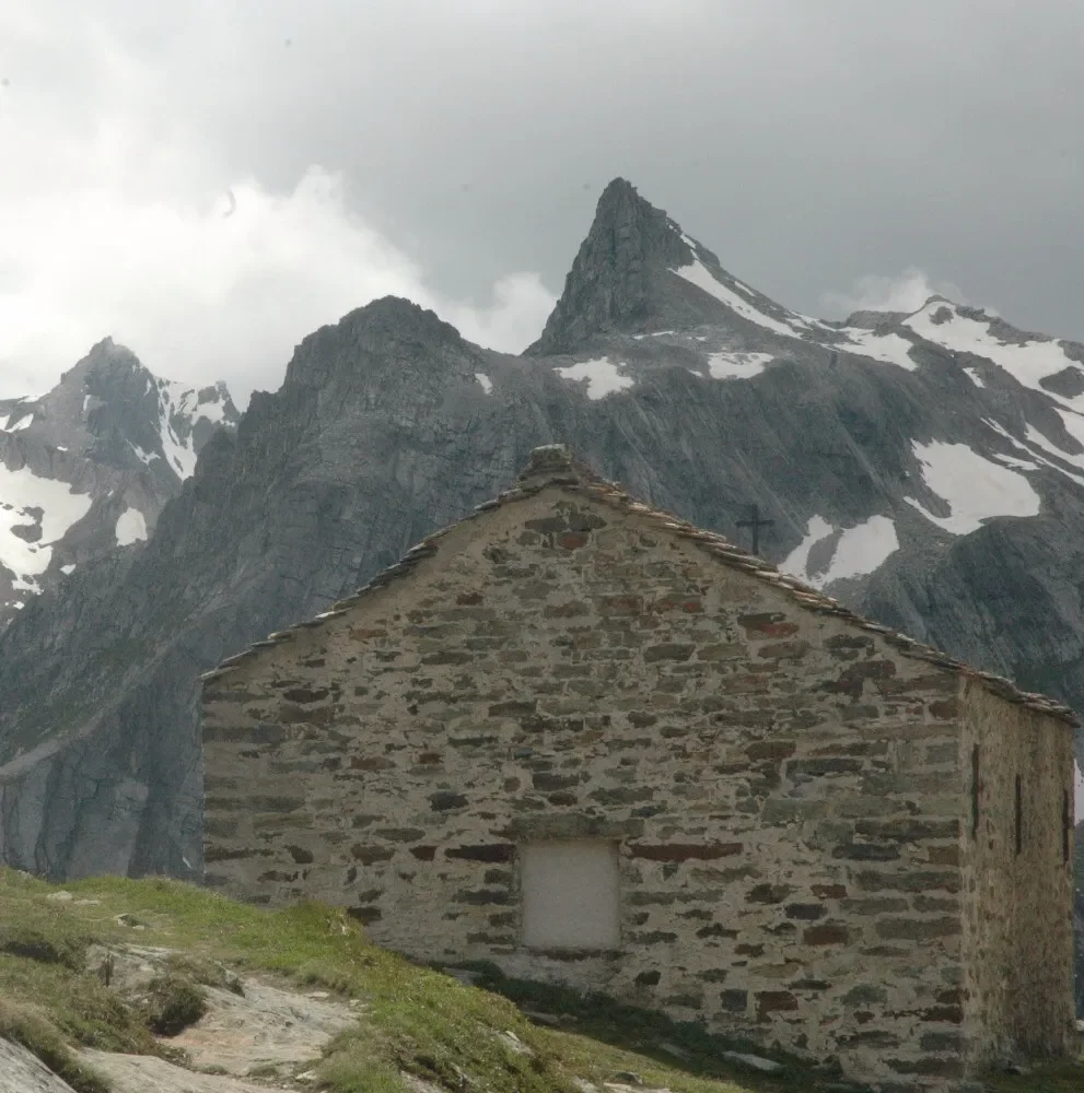 A stone house in front of snow-capped mountain peaks.