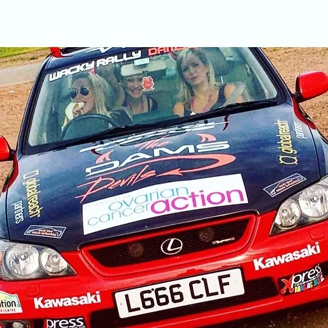 A rally car with three women inside, showing sponsor logos and a custom license plate.
