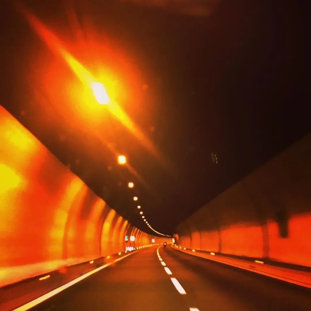 Inside a tunnel with orange lighting and a two-lane road curving ahead.