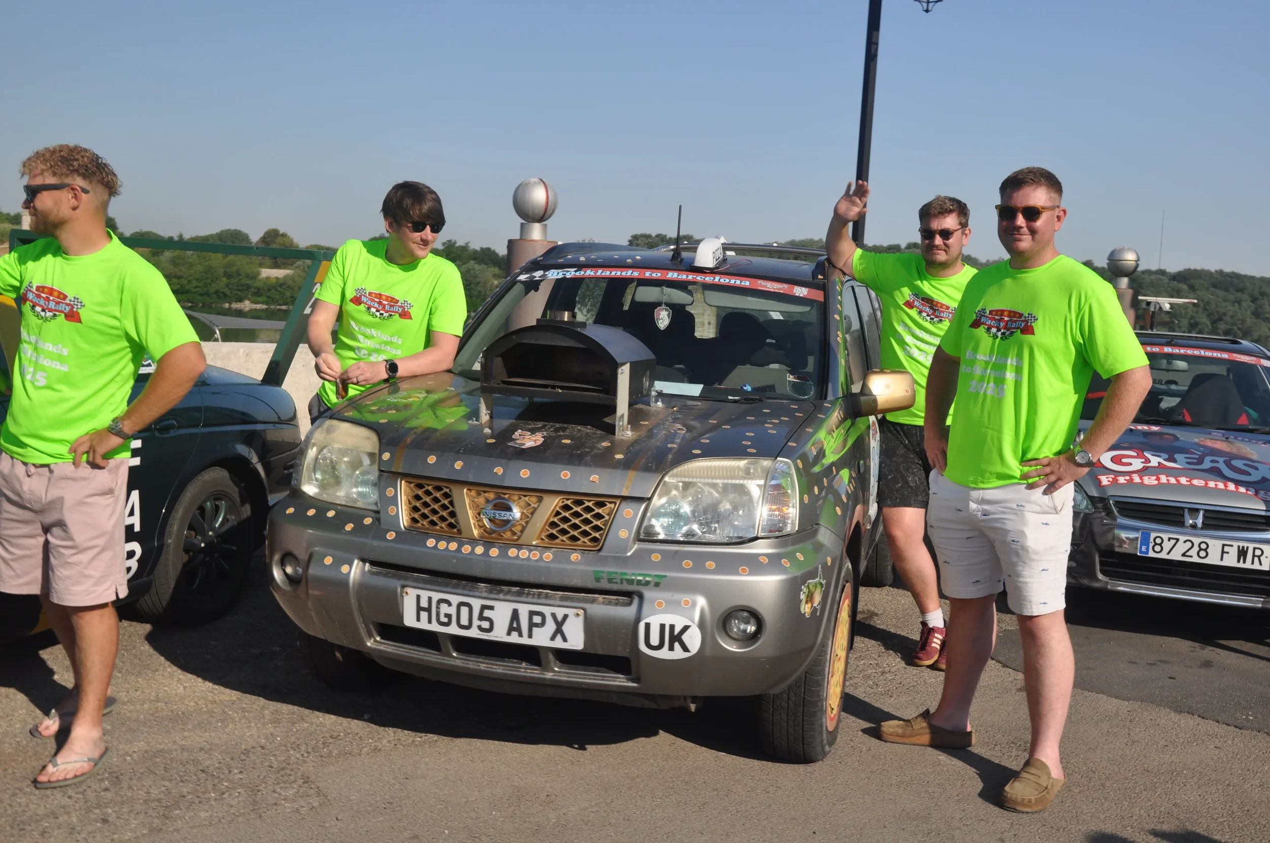 Group of people in bright green shirts standing beside race cars during a rally event on a sunny day.