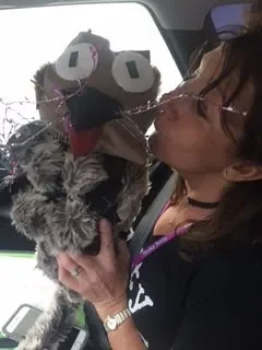 Person giving a kiss to a puppet dog with large eyes and a gray and black fur pattern.