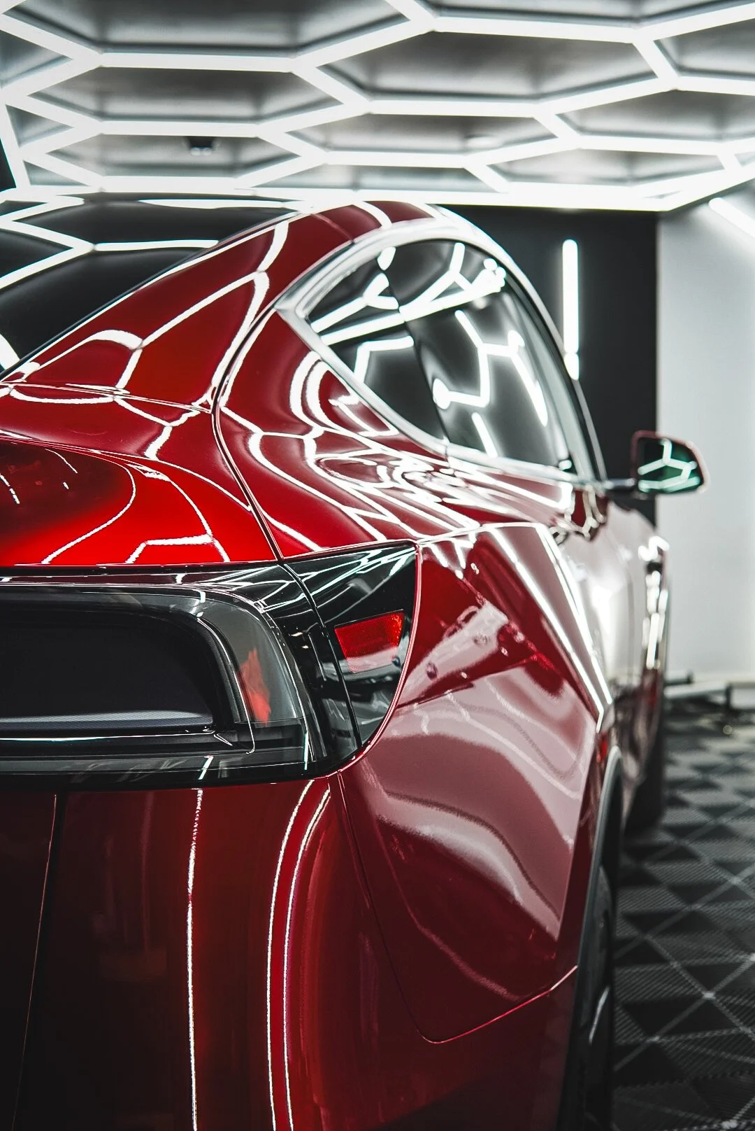 Close-up view of a shiny red luxury car inside a modern showroom with bright white geometric LED lighting panels on the ceiling.