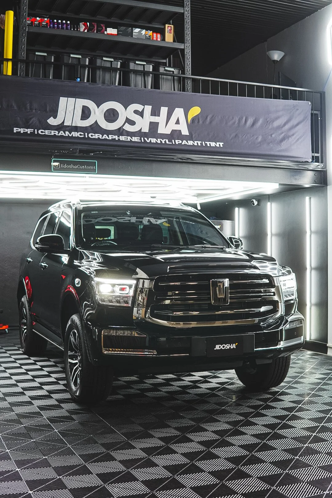 A black Honda SUV parked indoors, with a sign reading "Jidosha" and an interior background with shelving and lighting.