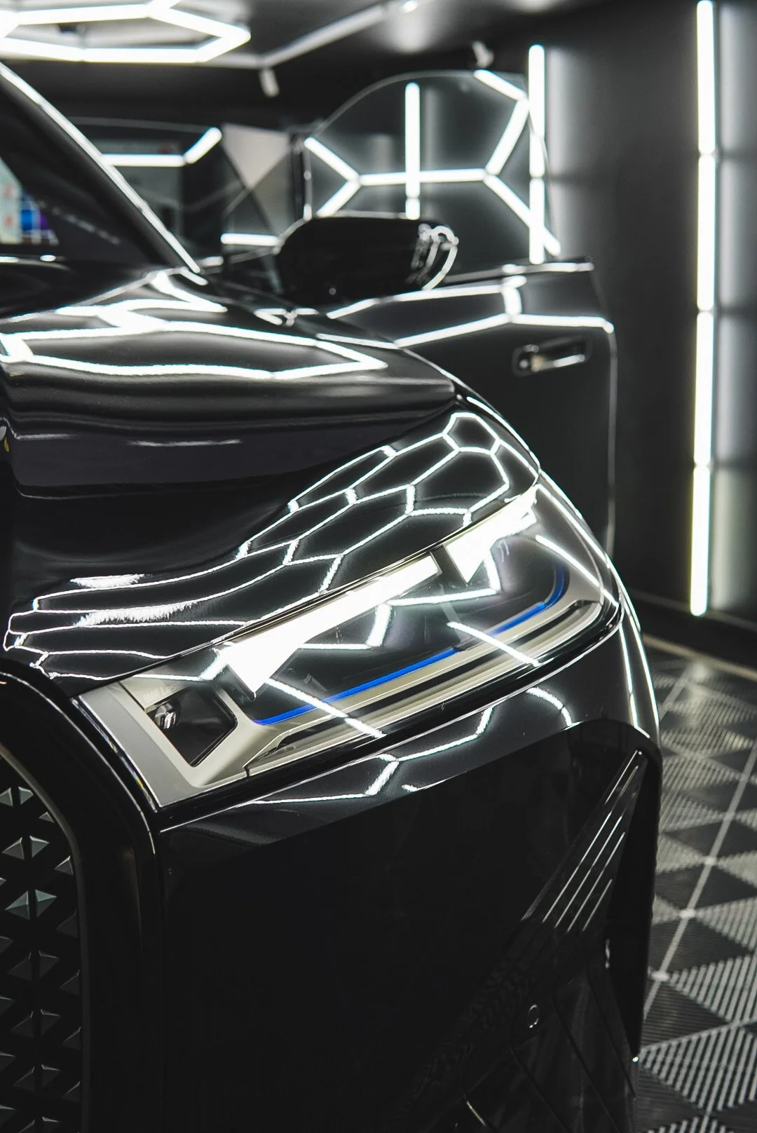 Close-up of a sleek, futuristic black car with illuminated geometric white light patterns reflecting off its surface inside a modern, high-tech garage.