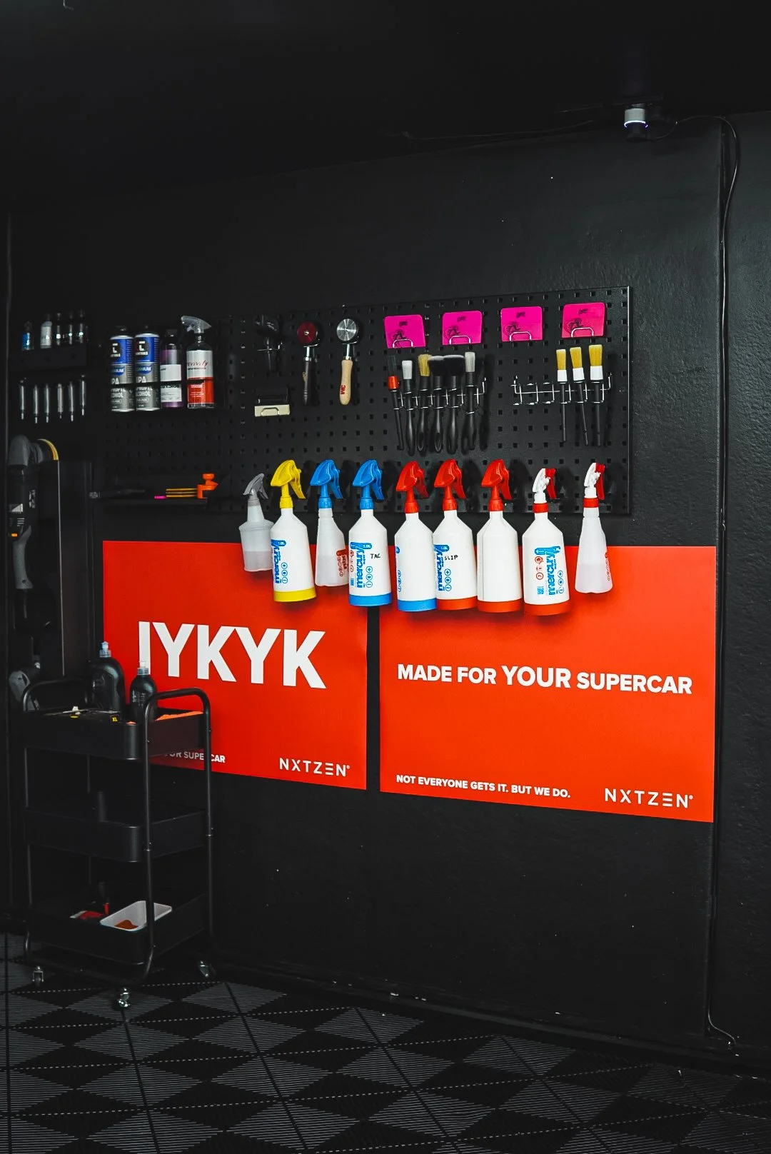 Tools and spray bottles organized on a black pegboard wall in a garage or workshop setting