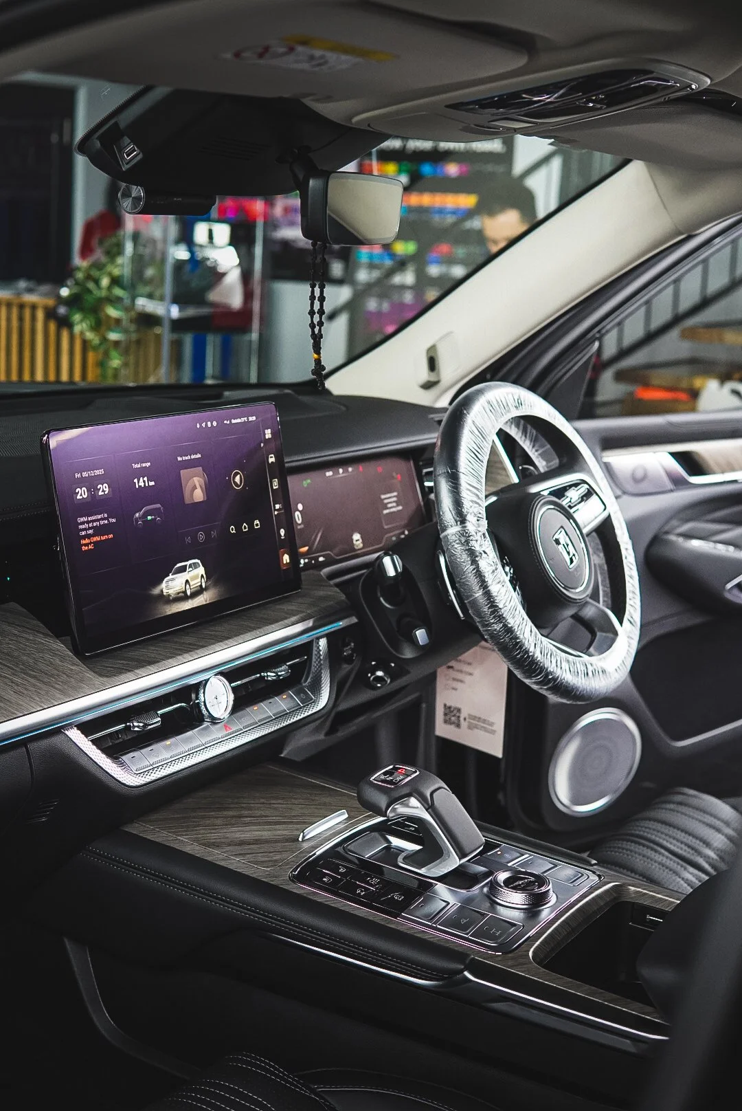 Interior of a modern vehicle showing the dashboard, steering wheel with a protective cover, digital display, and center console with gear shift.