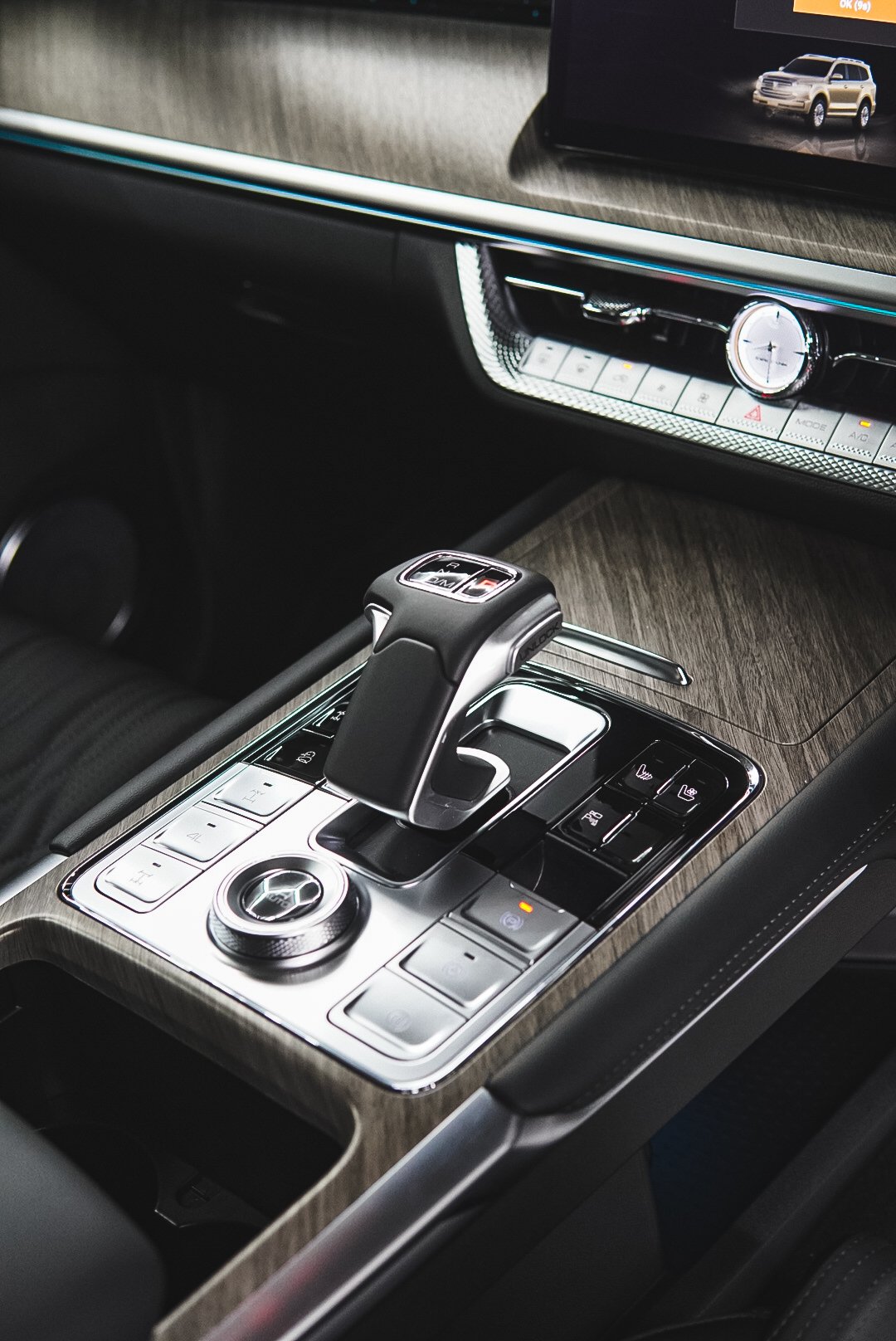 Interior of a luxury vehicle showing a gear shift, control buttons, and a digital display screen with an image of an SUV.