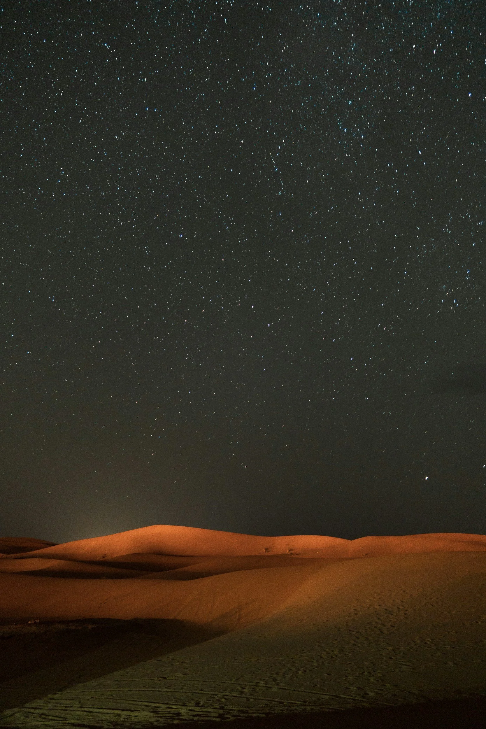 Nighttime desert scene with sand dunes and a clear, starry sky overhead.