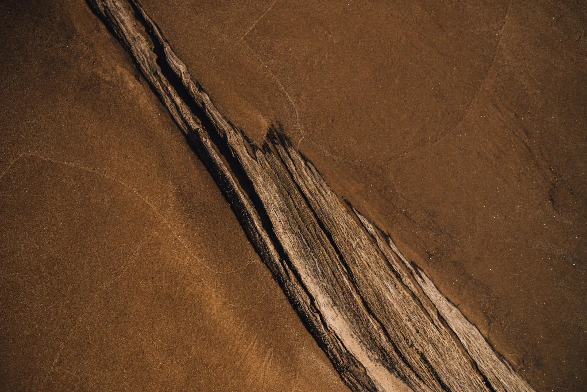 Close-up aerial view of a long, narrow crack in a dry, cracked earth surface, with parallel ridges along the crack.