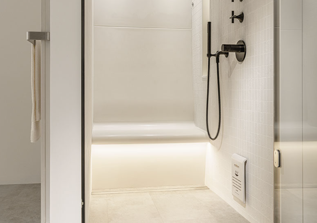 Minimalist walk-in shower with black fixtures, beige tiles, and a white wall, featuring a towel on a hook on the left side.