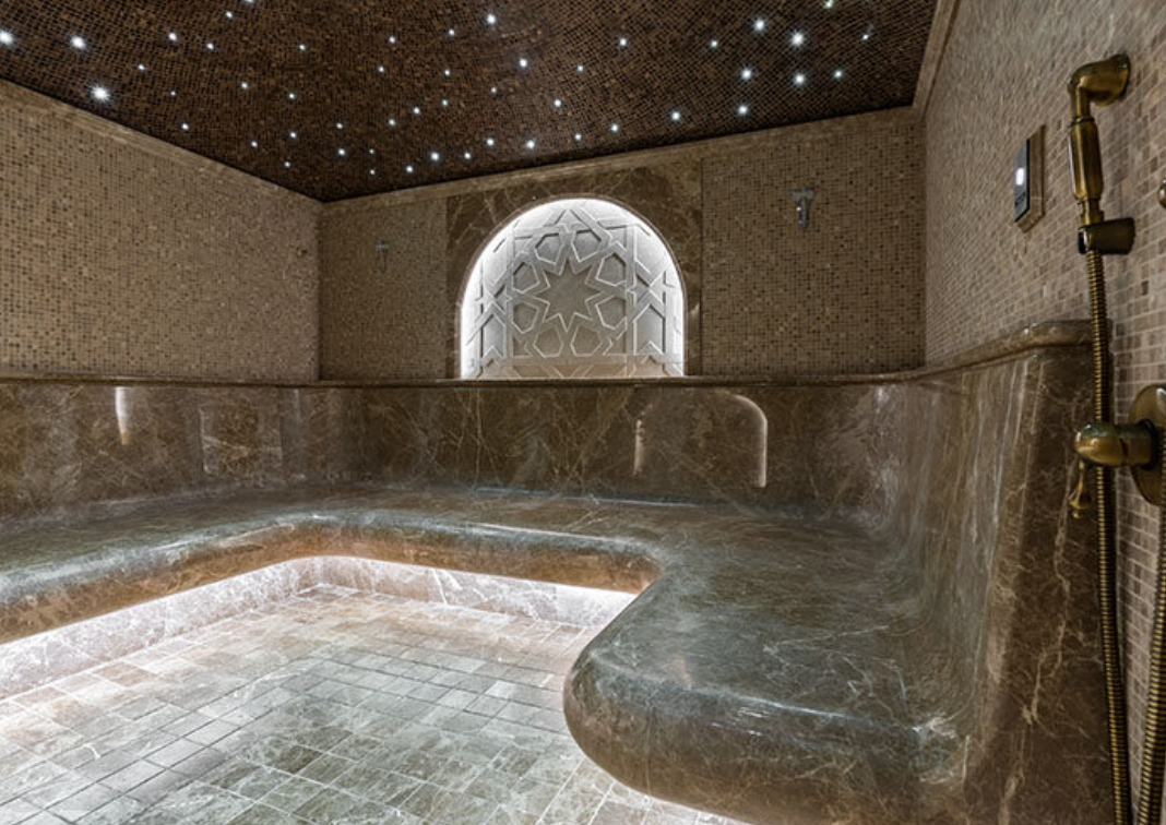 Luxurious steam room with marble benches, starry ceiling lights, decorative window, and gold shower fixtures.
