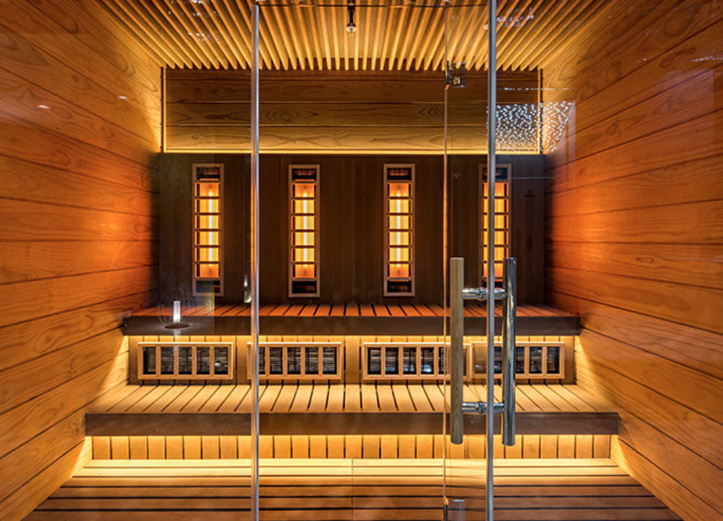 Interior of a sauna room with wooden walls, benches, warm lighting, and a glass door.