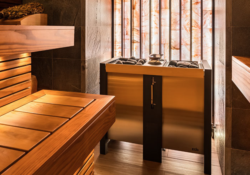 A wooden slatted bench and a foot spa with stones at a spa or wellness center, illuminated by a softly glowing backlit onyx wall.