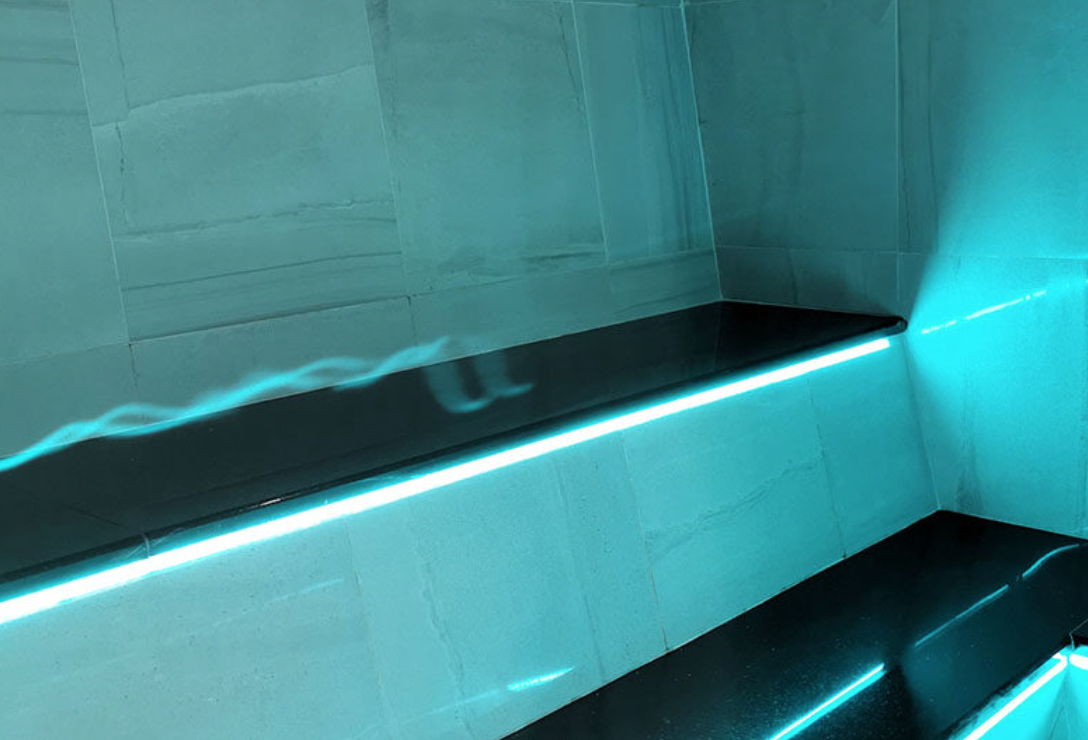 Modern interior with illuminated blue neon light strips along and below black edges of wall-mounted shelves, against light-colored tiled wall.