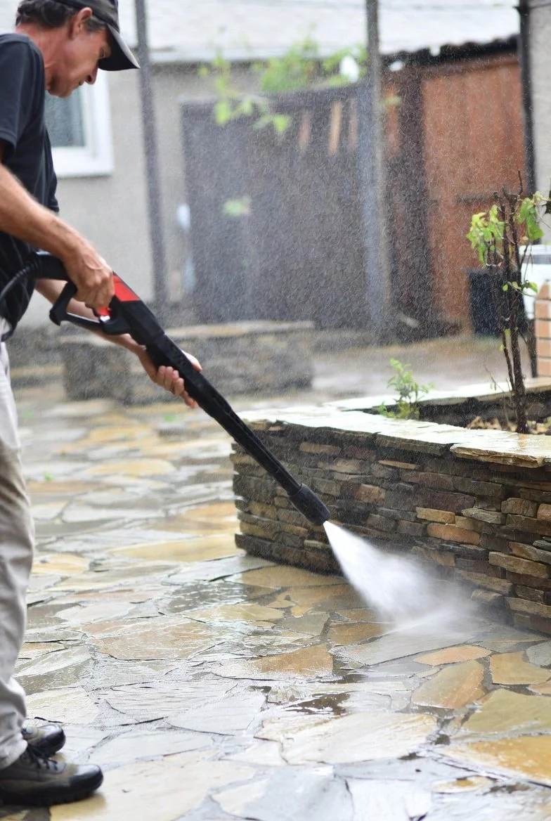 Person using a pressure washer to clean stone patio outdoors