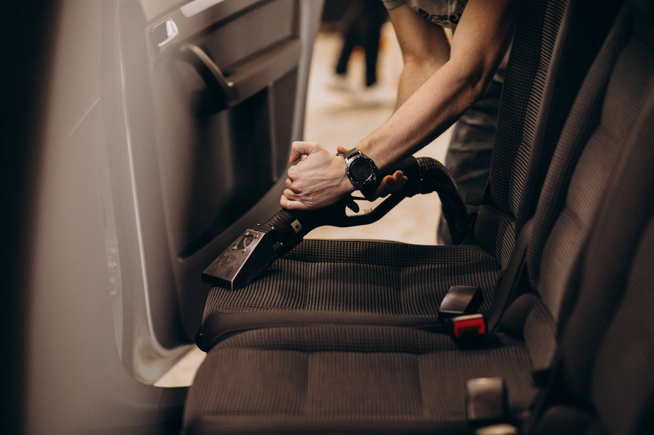 Person cleaning airplane seat with handheld vacuum, wearing a wristwatch.