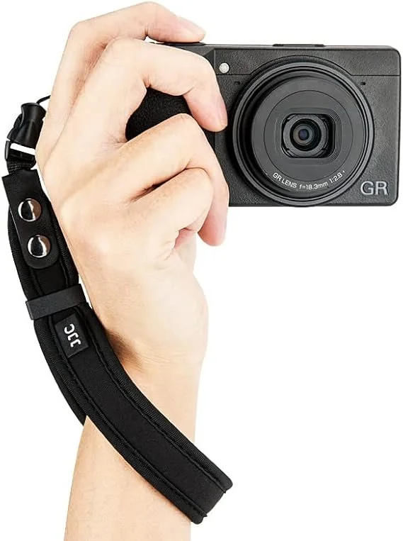 Mano che tiene una fotocamera digitale compatta con cinturino nero