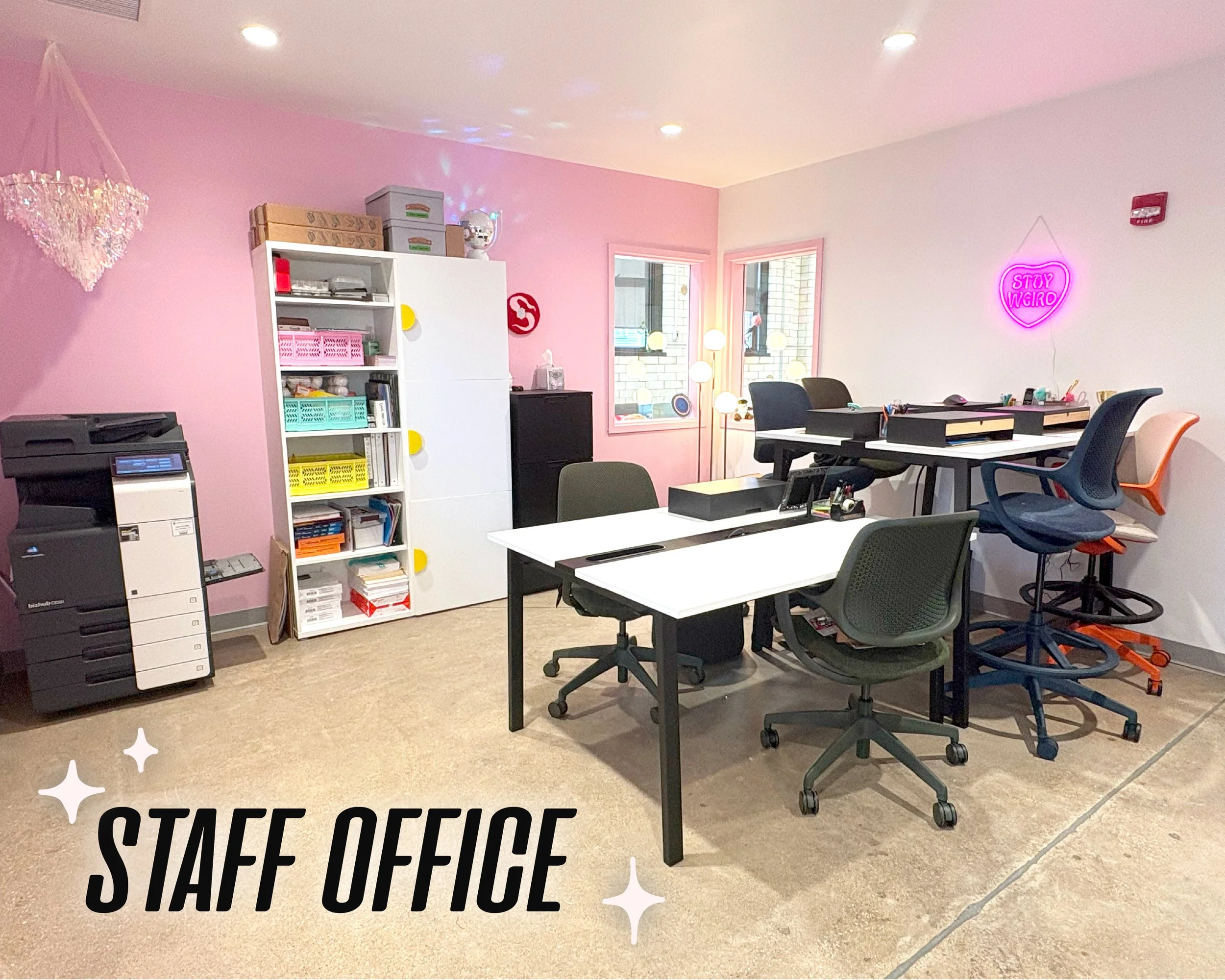 Graphic text reads "Staff office" over an immage of an office space with a pink accent wall. A pink neon sign reading "Stay Weird" decorates the wall. A printer and a shelf with other office supplies are visible.