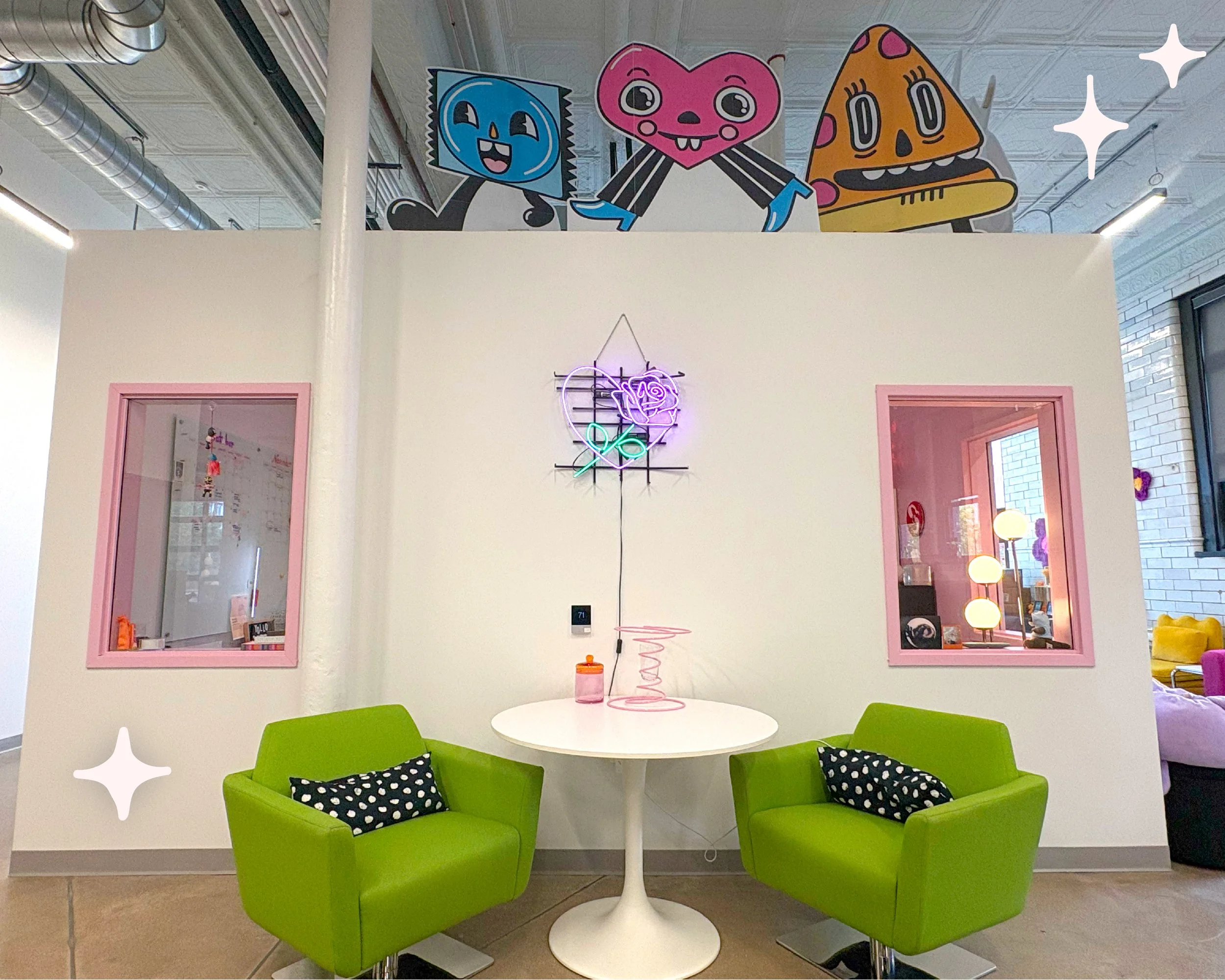 A differnt view of the "Cental Event Space" reveals more seating options, green upholstered chairs and a white table are visible, along with neon sign depicting a rose on the wall. Several illustrated character standees are also visible. 